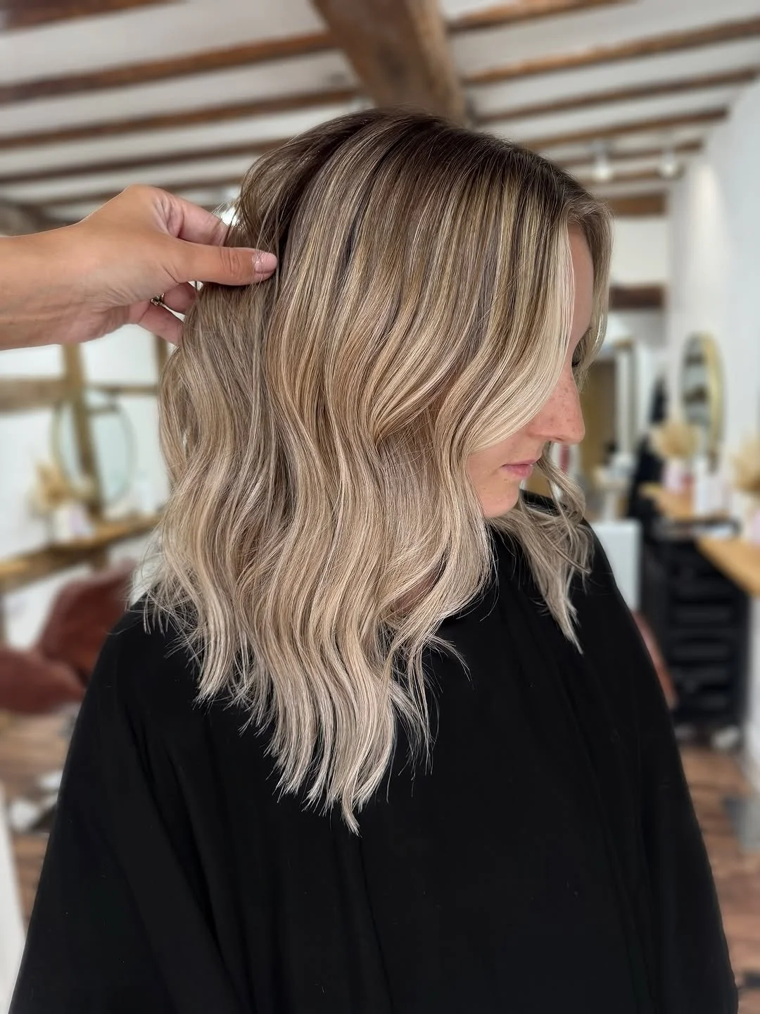 A woman with blonde, wavy hair receiving a hair styling or coloring treatment in a salon.