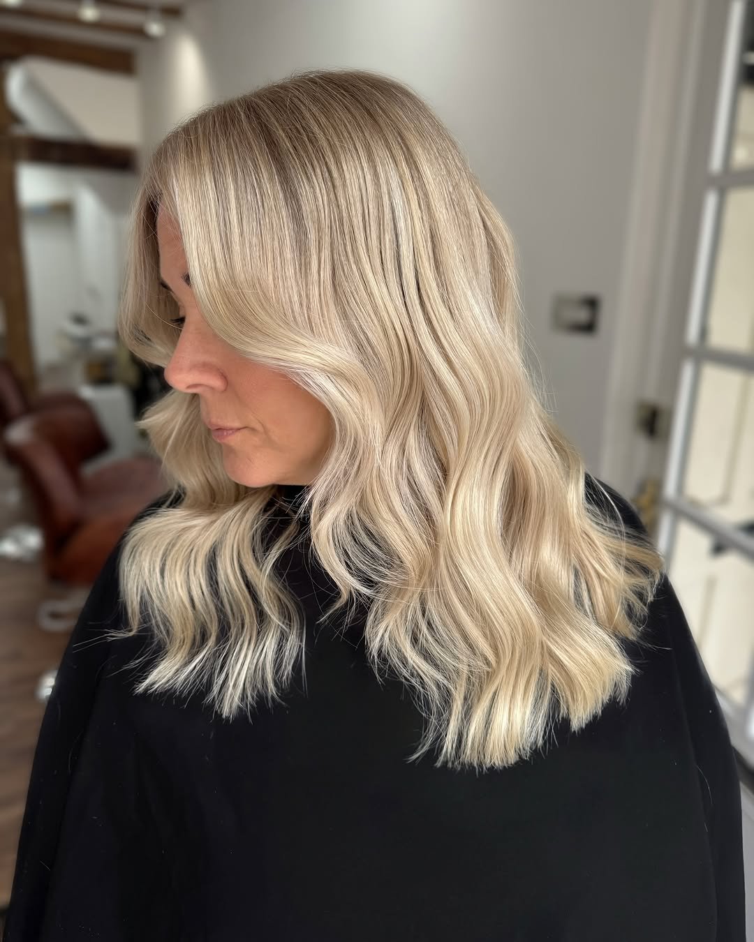 Woman with long, wavy blonde hair in a salon or home setting, wearing a black top.