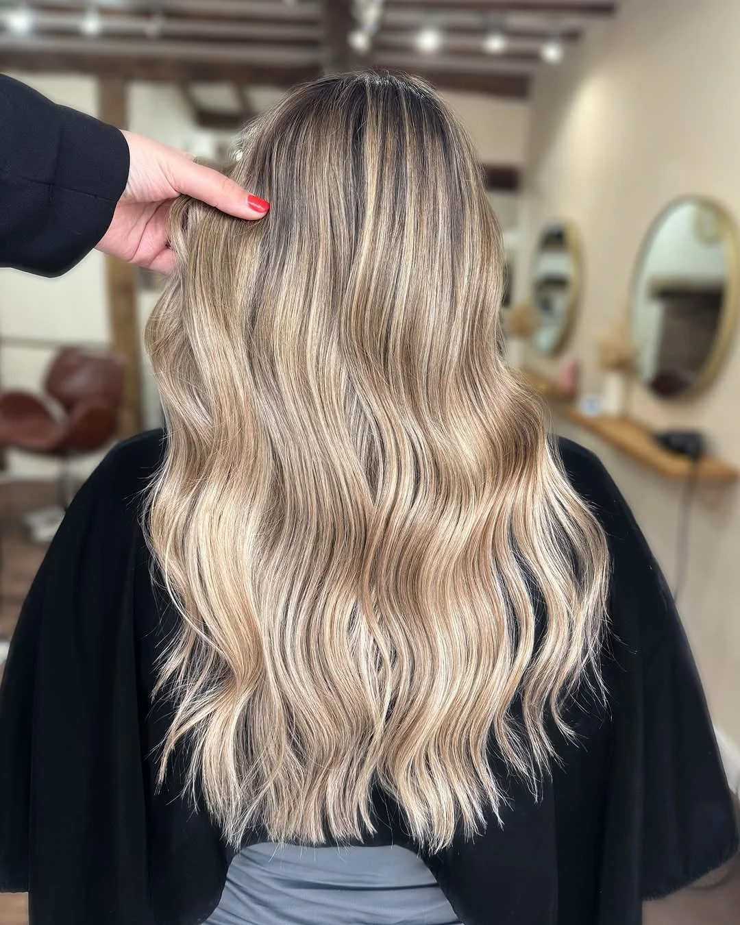 Back view of a woman with long, wavy blonde hair inside a salon.