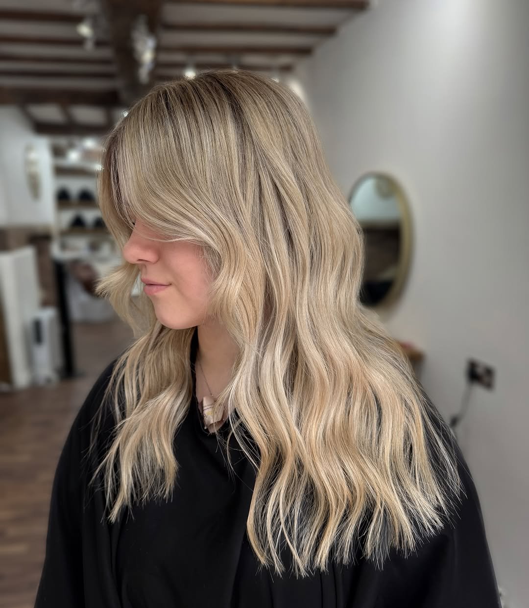 Side view of a woman with shoulder-length blonde wavy hair in a salon.