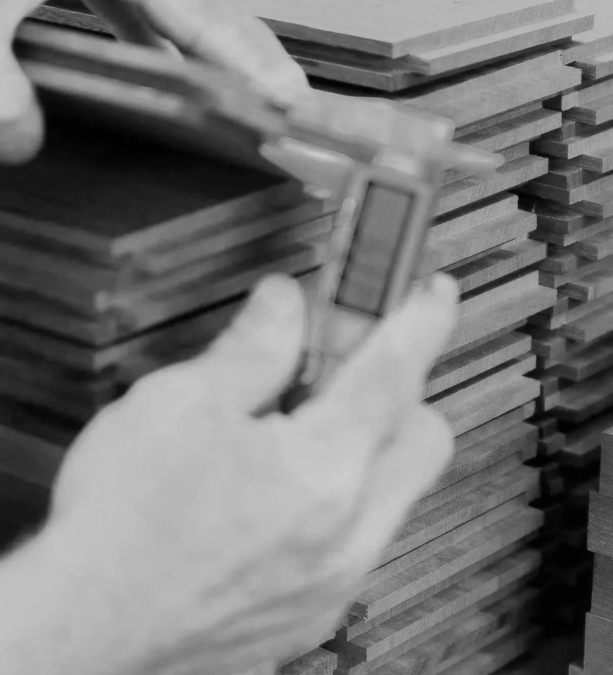 Hands measuring a stack of wooden planks using a caliper.