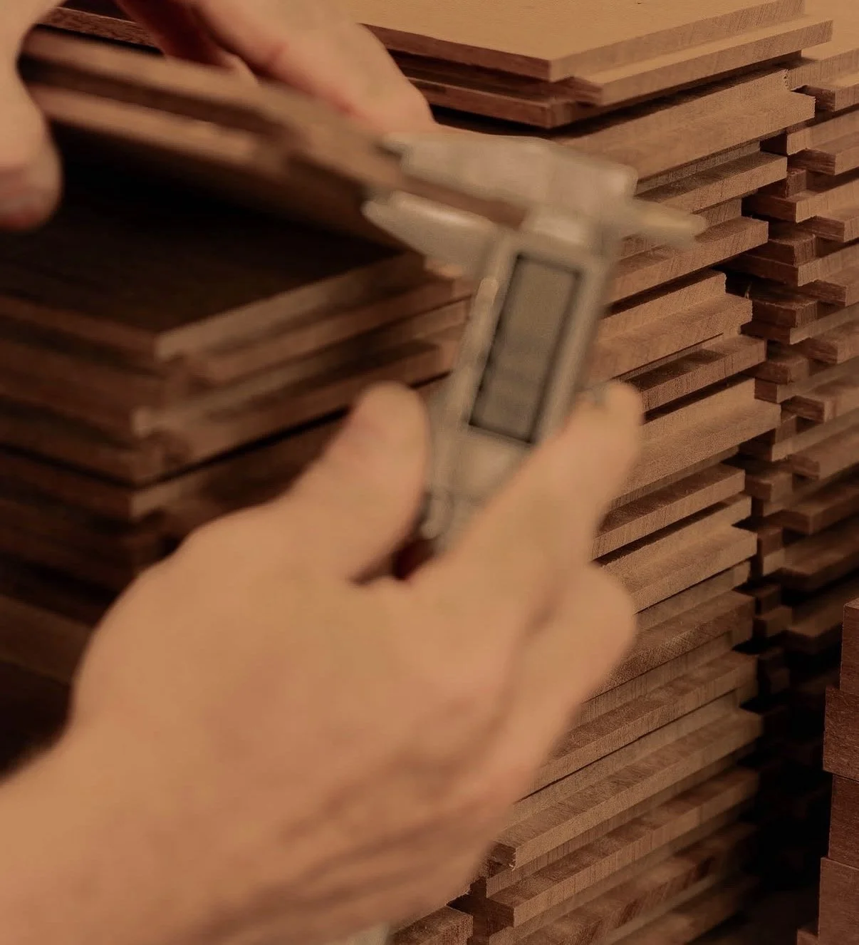 Hands measuring a stack of wooden planks using a caliper.
