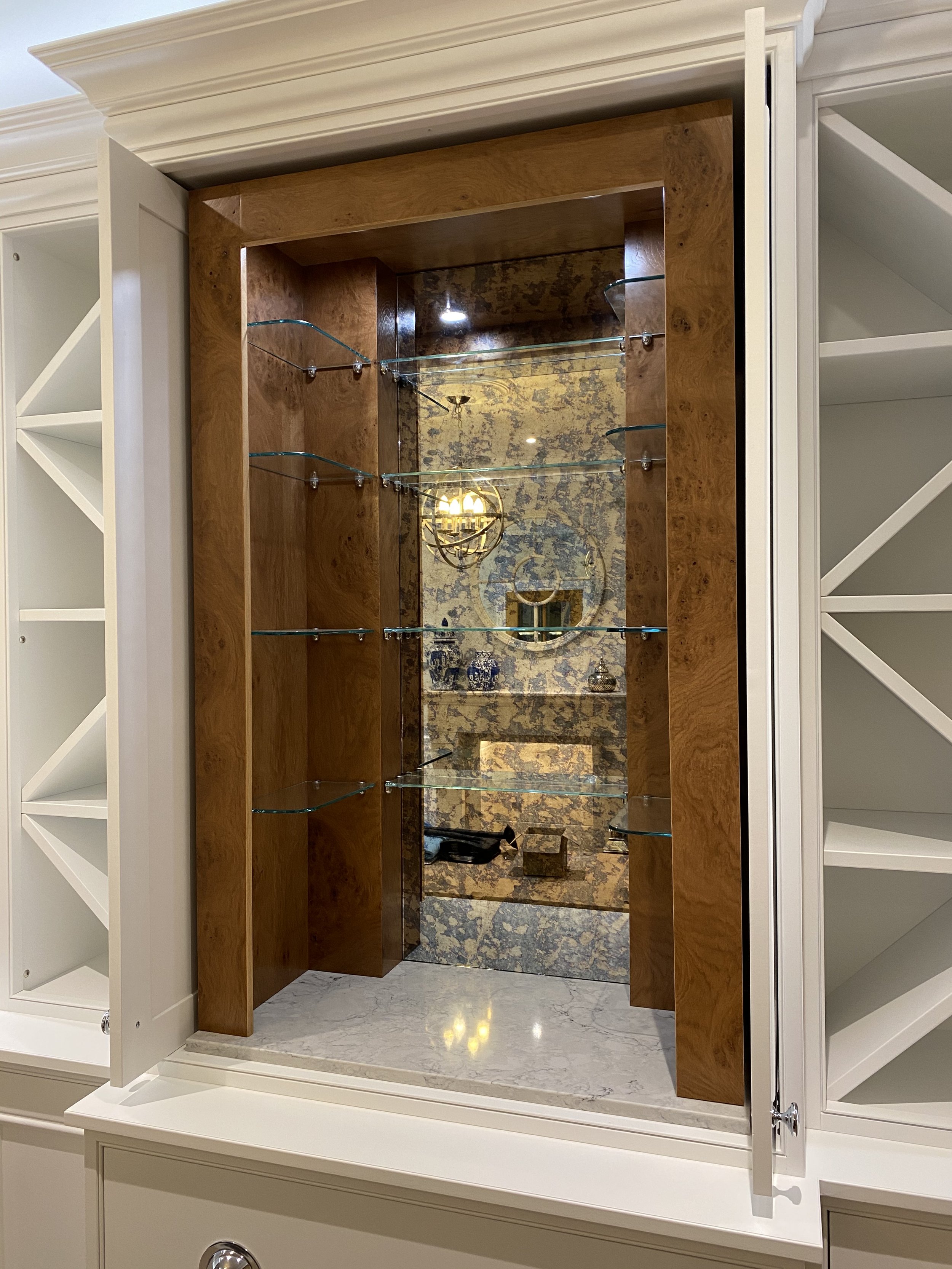 A mirror framed in wood with glass shelves, bordered by white cabinetry with shelves and a marble countertop underneath.