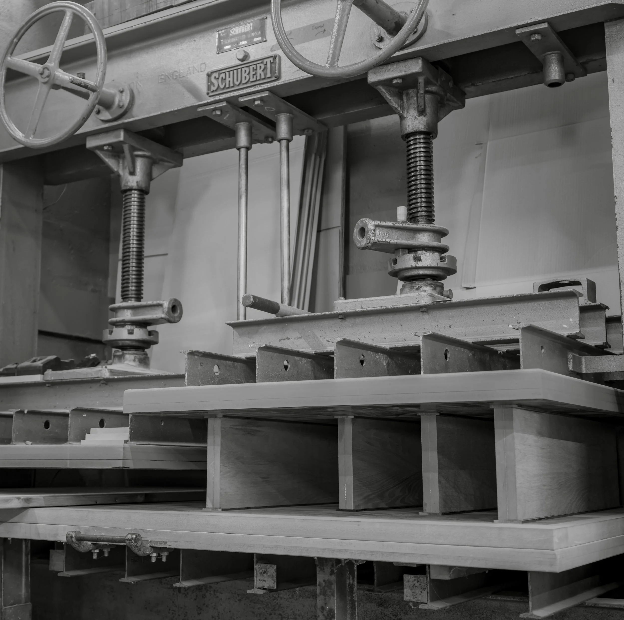 A close-up view of a vintage industrial machine labeled "Schubert" with hand cranks, screws, gears, and levers, made of metal and showing signs of use.