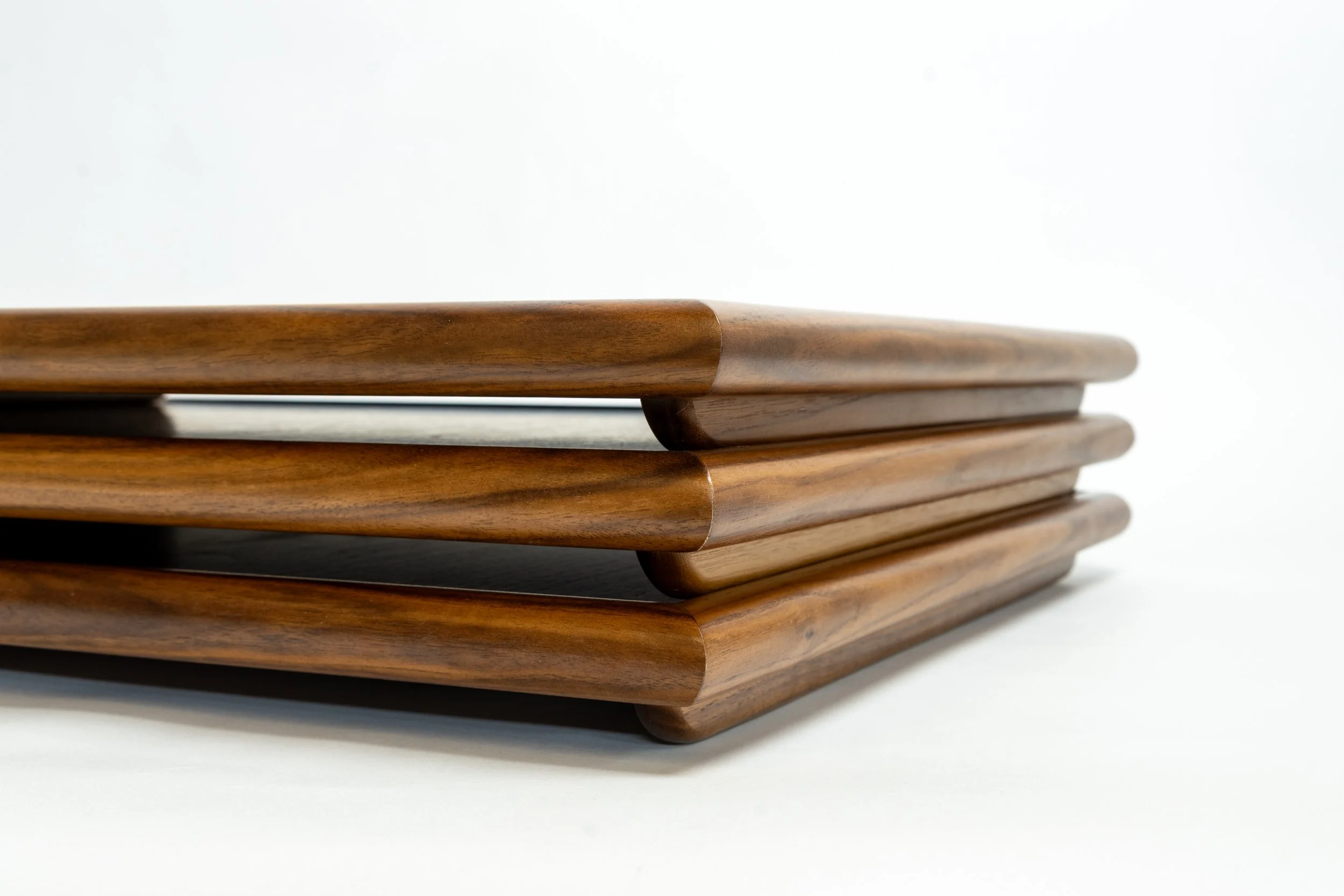 Close-up of a stack of wooden cutting boards with rounded edges on a white background.