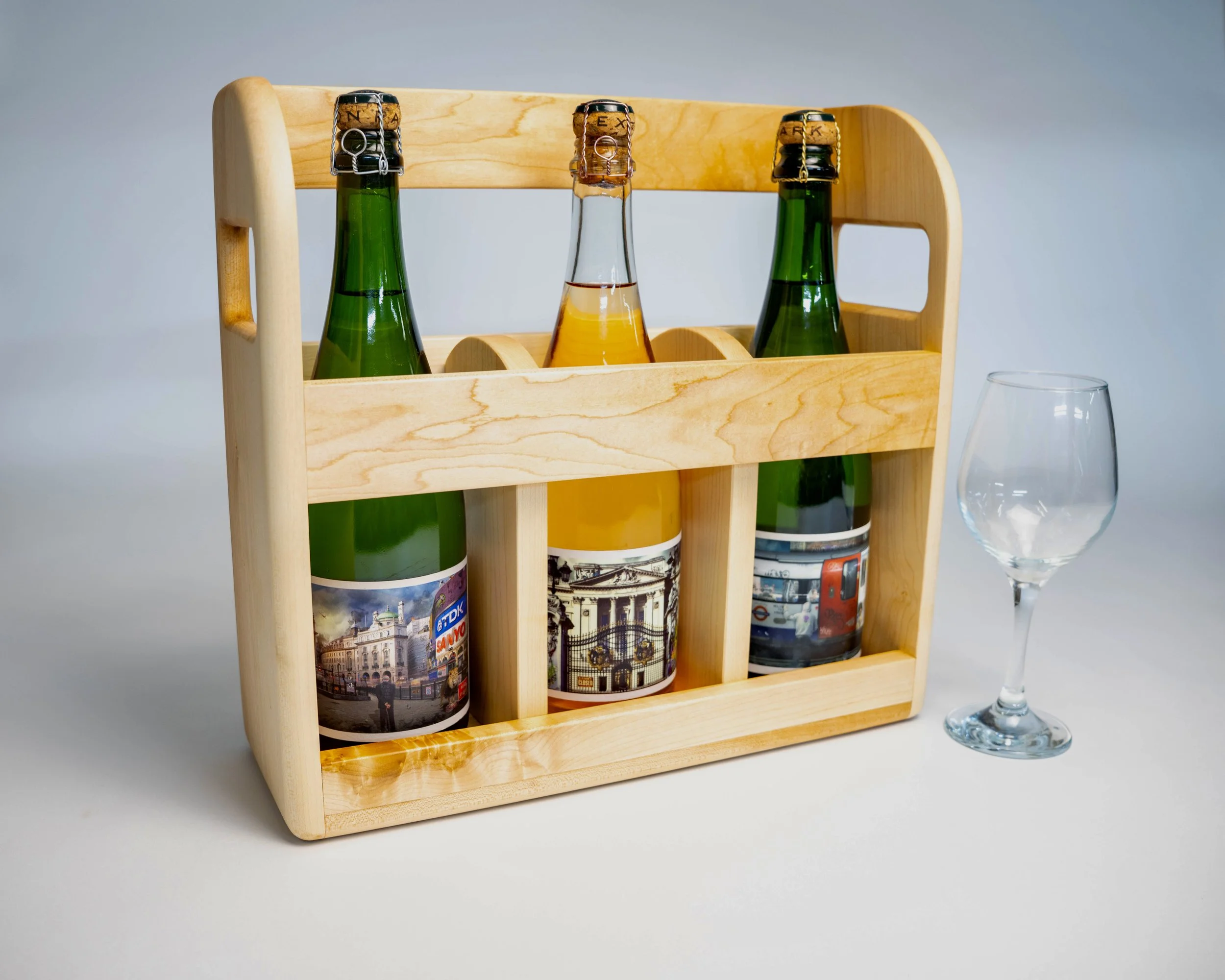 A wooden crate holding three bottles of beverage, with an empty wine glass beside it.