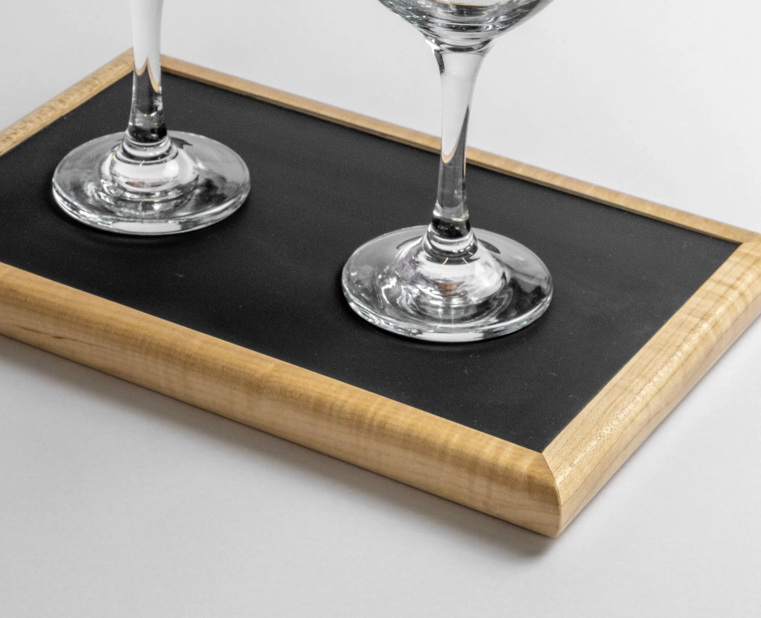 Close-up of two empty wine glasses on a black chalkboard tray with a wooden border, placed on a white surface.