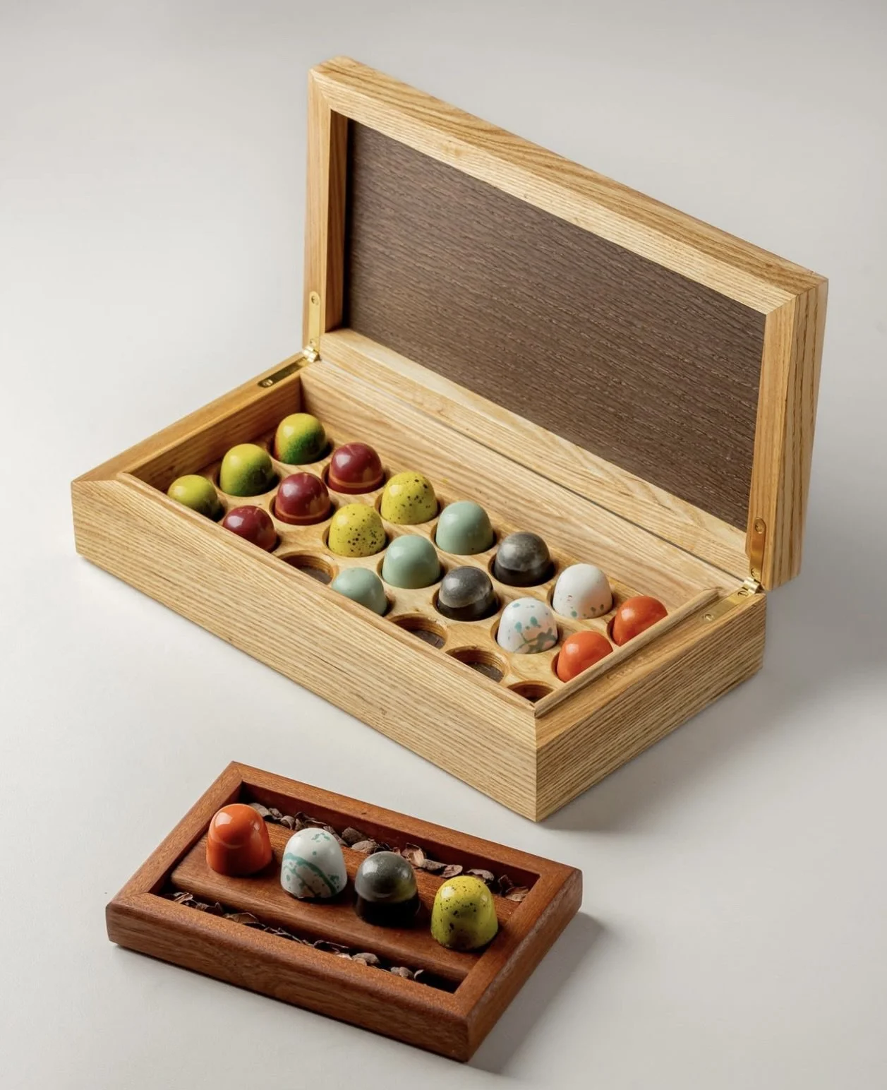 A wooden box with a hinged lid, containing colorful, speckled ceramic eggs arranged in a grid.