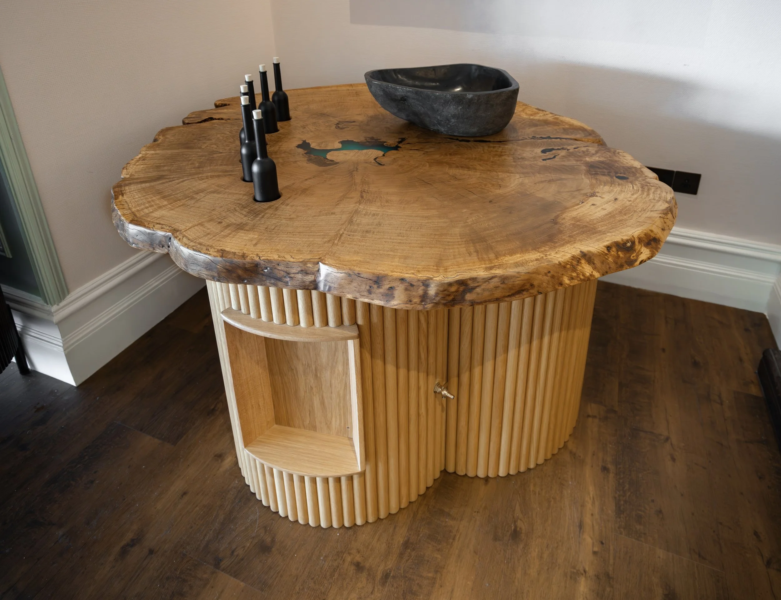 Oak table with Epoxy resin table top.  Recessed black bottles with cork caps and a granite sink 