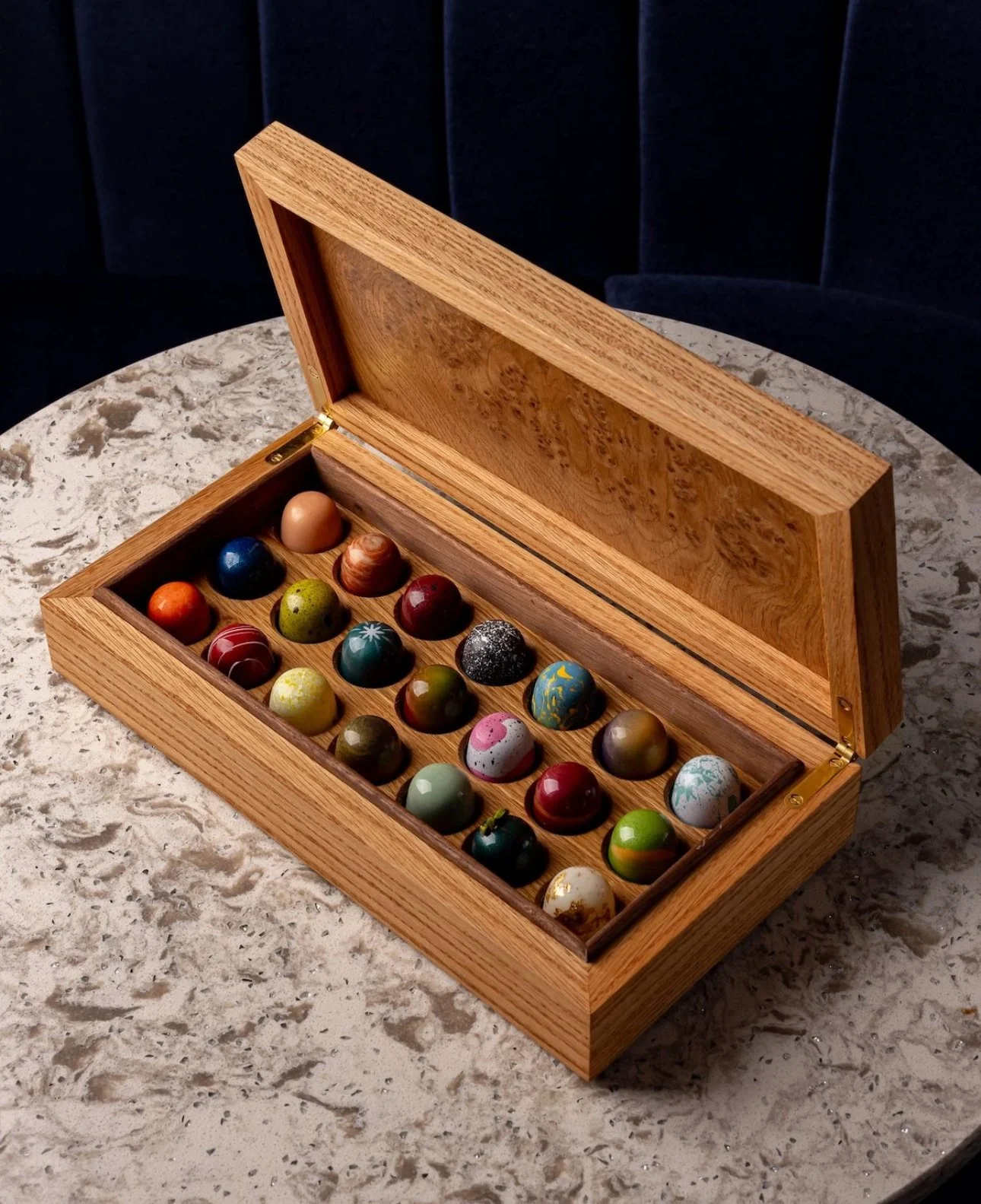 A wooden box with a glass lid, filled with colorful decorative eggs, sitting on a marble table.