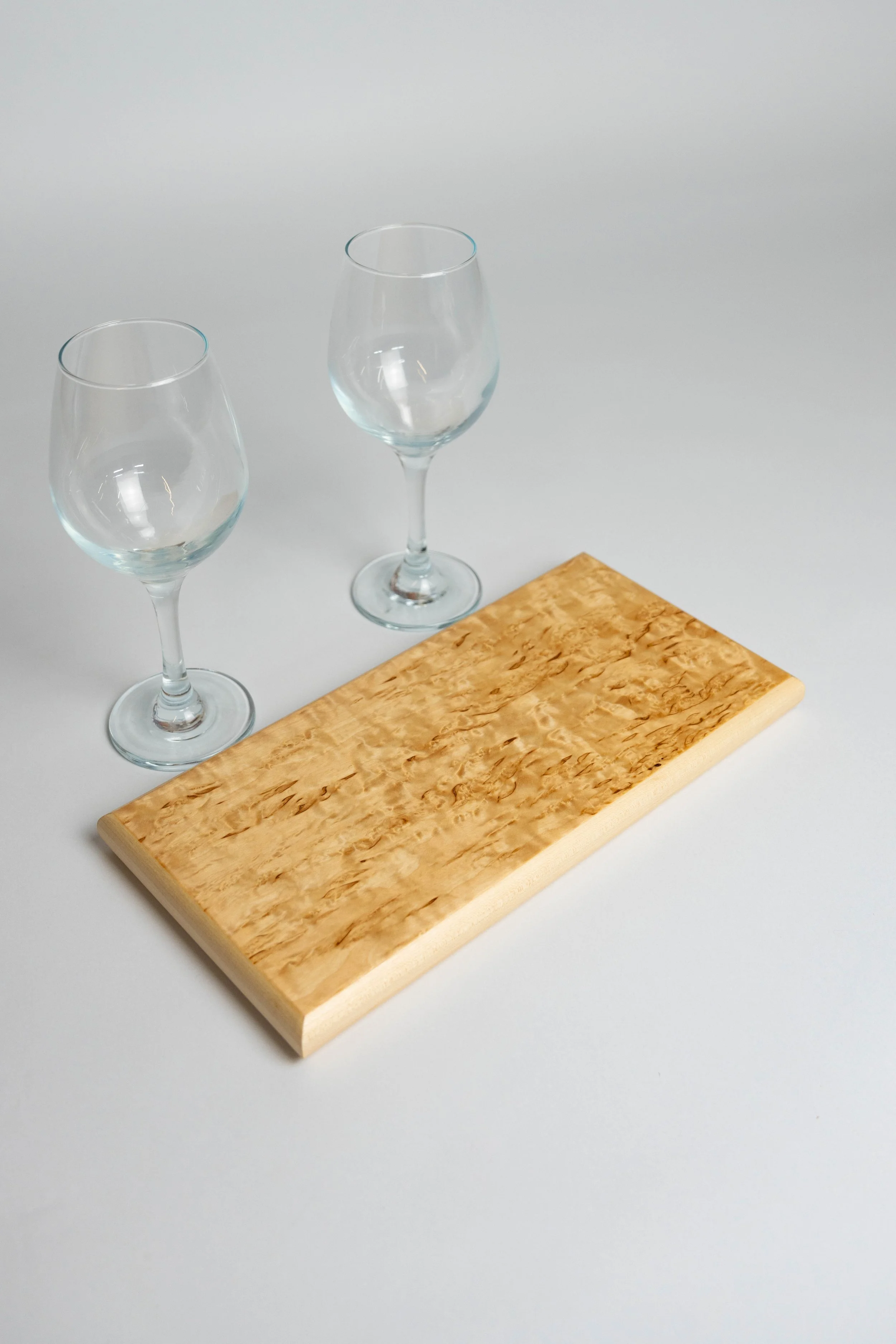 Two empty wine glasses and a wooden cutting board on a white surface.