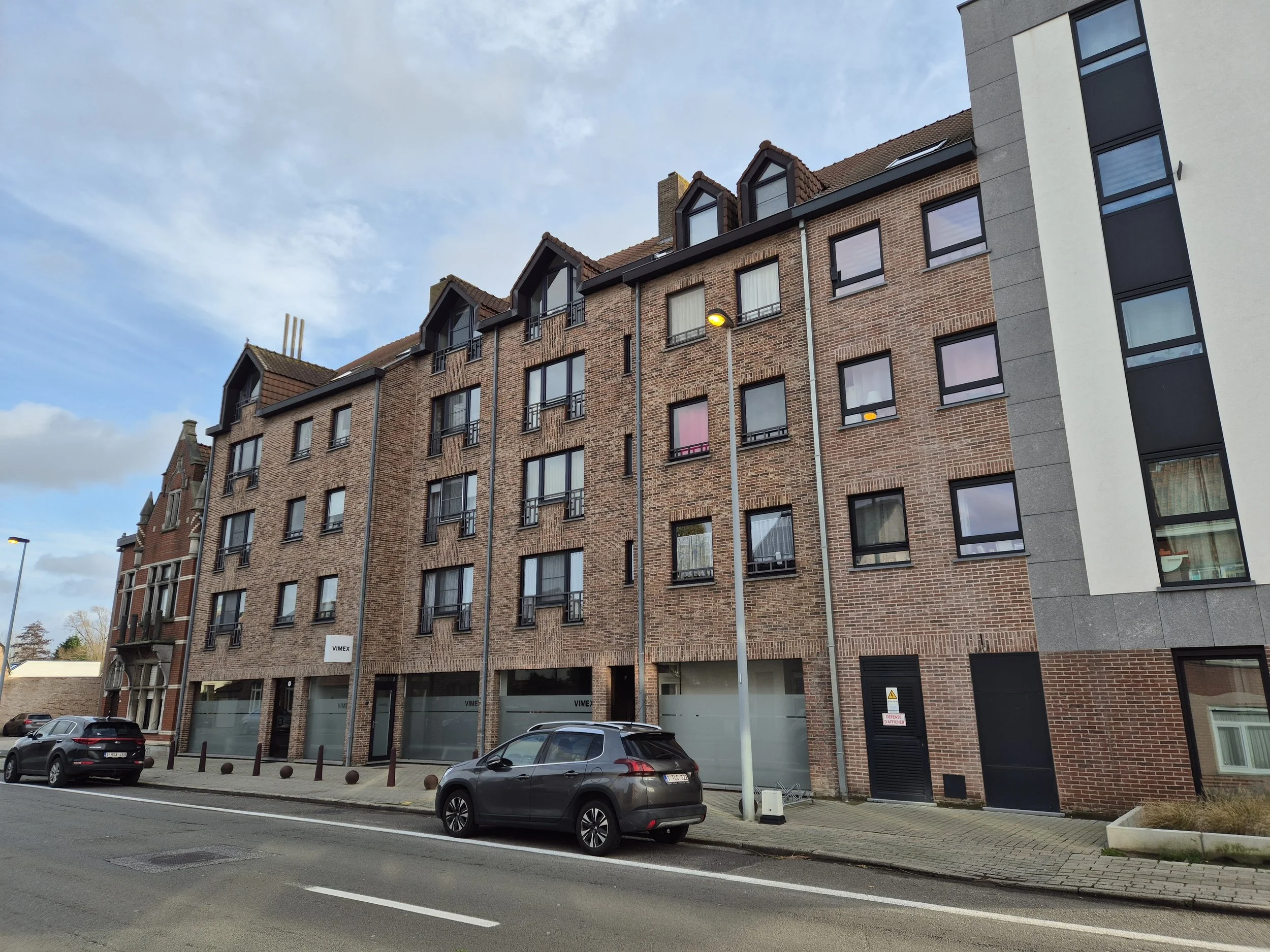 Bouw van een modern appartementengebouw met meerdere verdiepingen in een stedelijke omgeving, met geparkeerde auto's op de straat voor het gebouw.