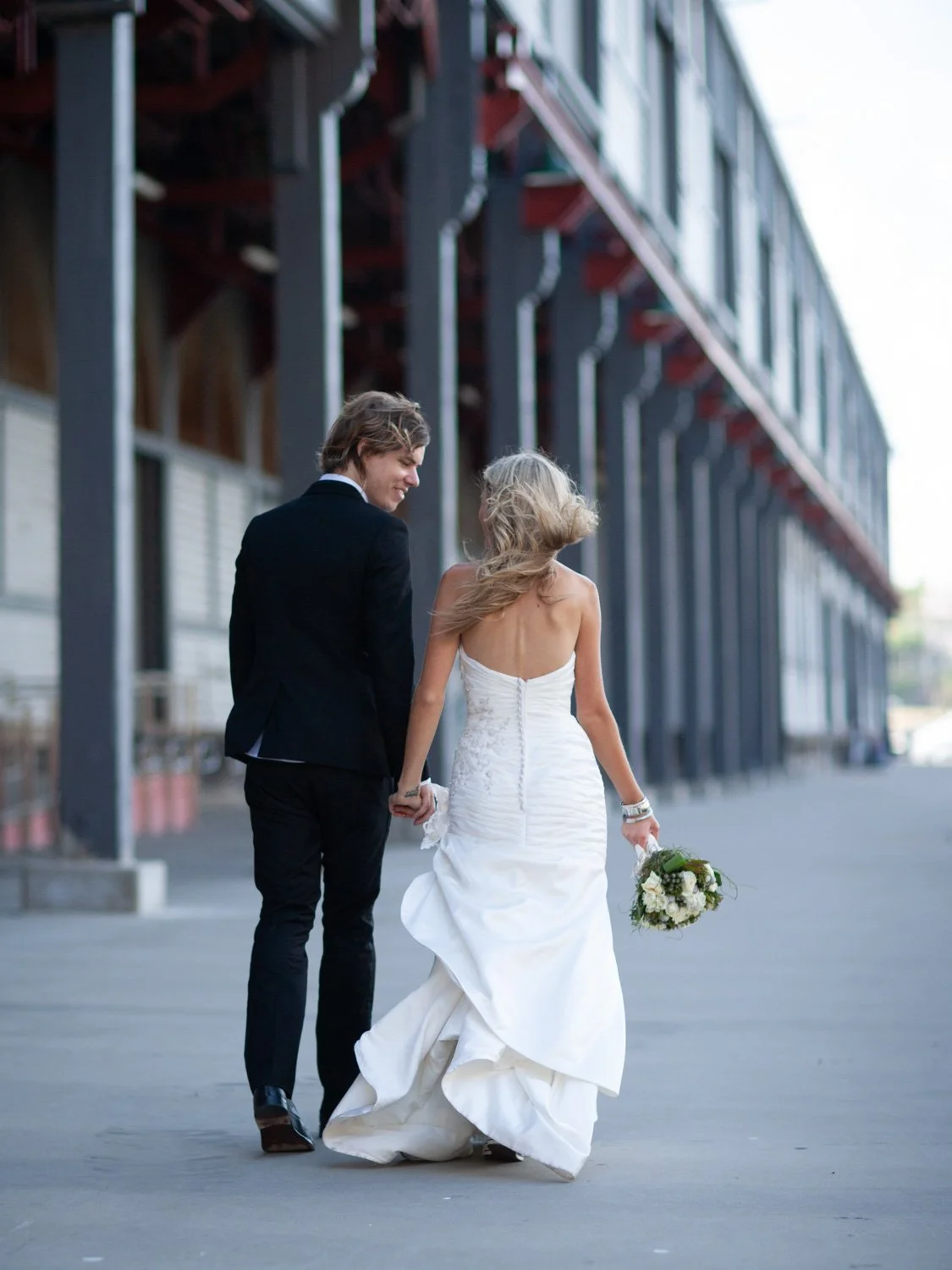 Bride and groom hand in hand walking away on Walsh Bay pier