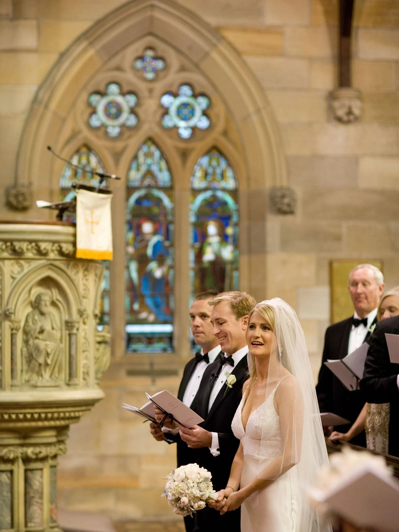 Bride and groom singing with stained glass windows behind them, All Saints Anglican Church Woollahra