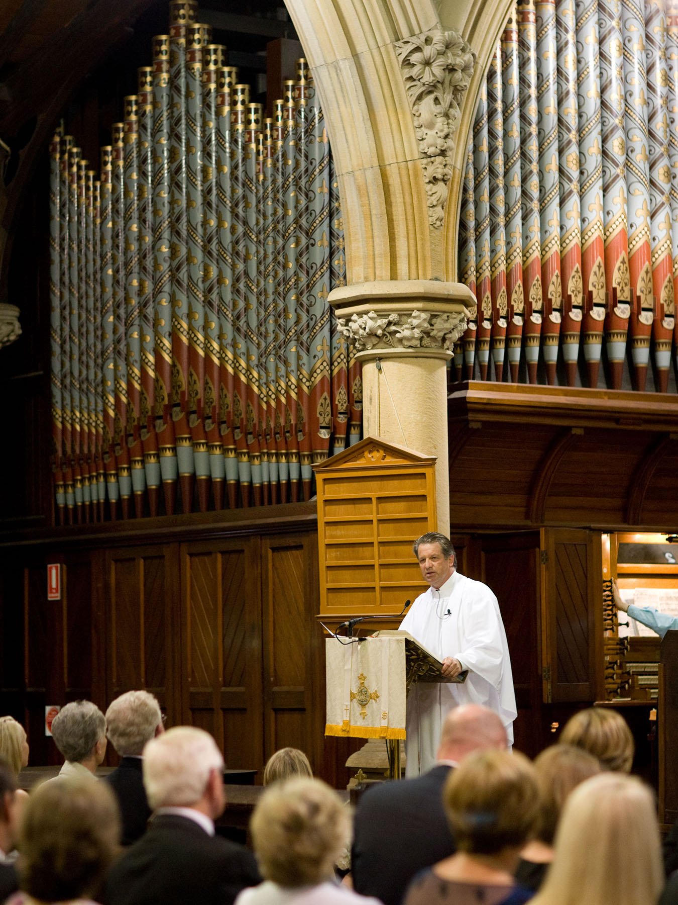 Minister officiating the wedding ceremony beneath the pipe organ at All Saints Anglican Church Woollahra