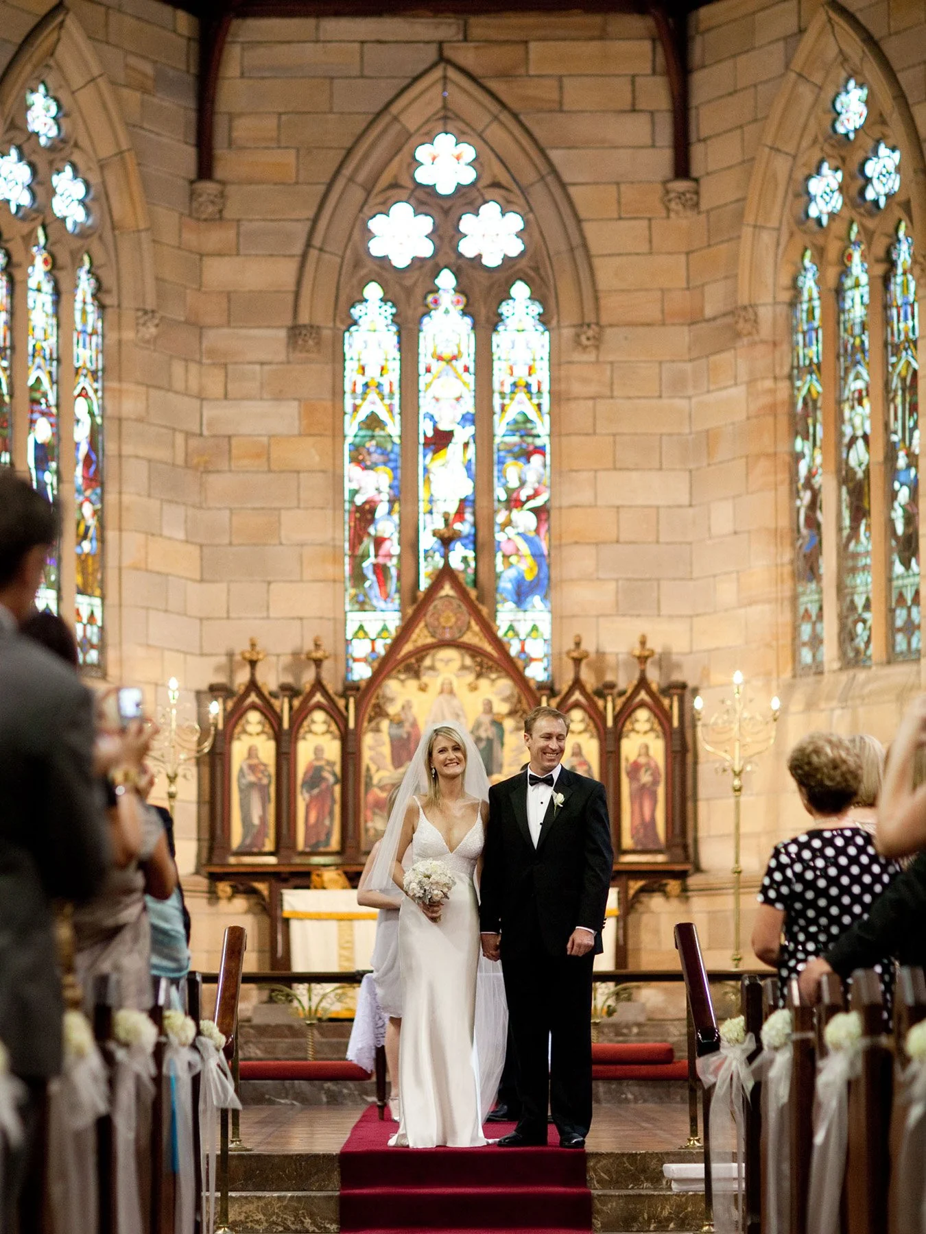 Bride and groom at the altar with stained glass windows behind them, All Saints Anglican Church Woollahra