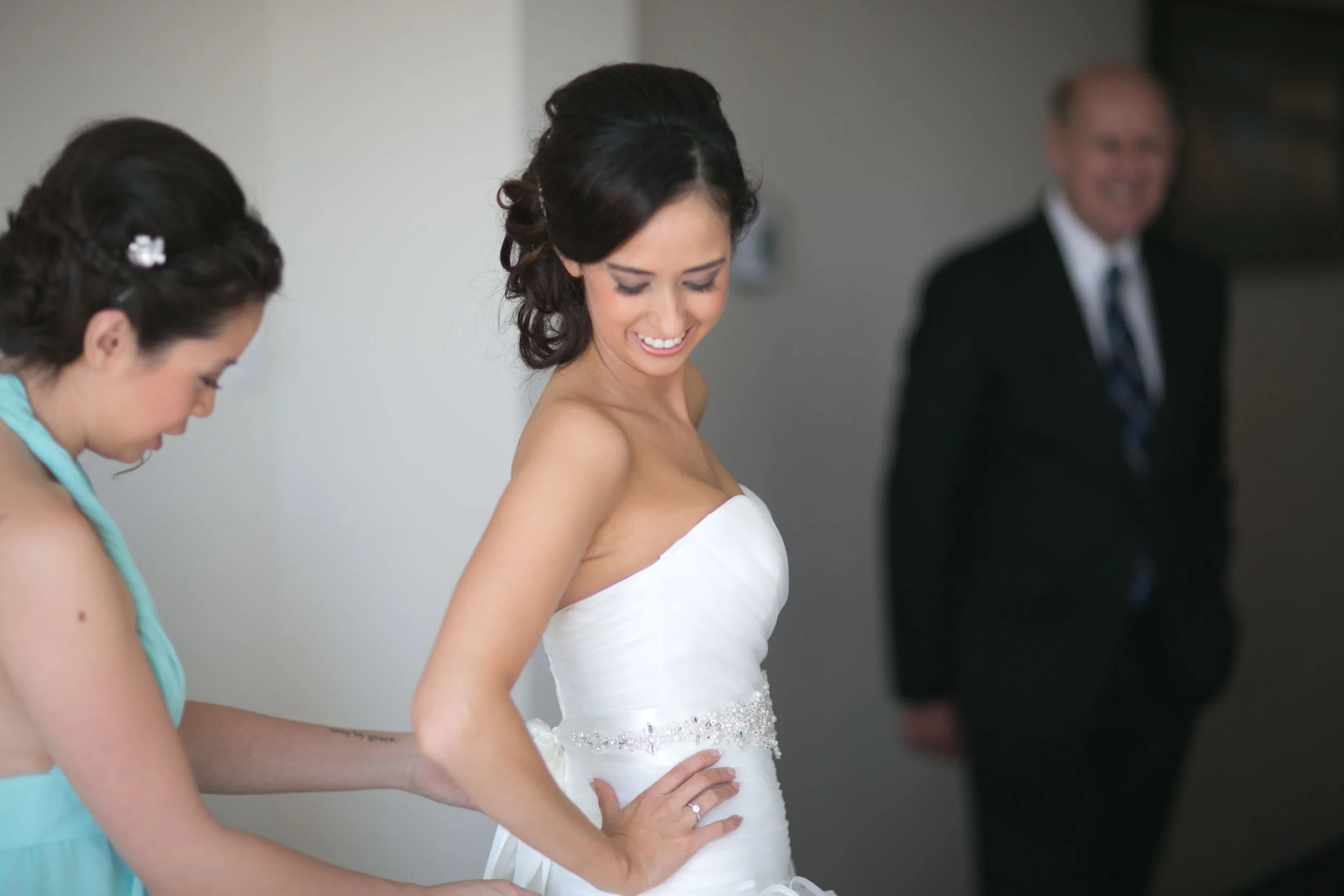 Bride with bridesmaid and father during final preparations