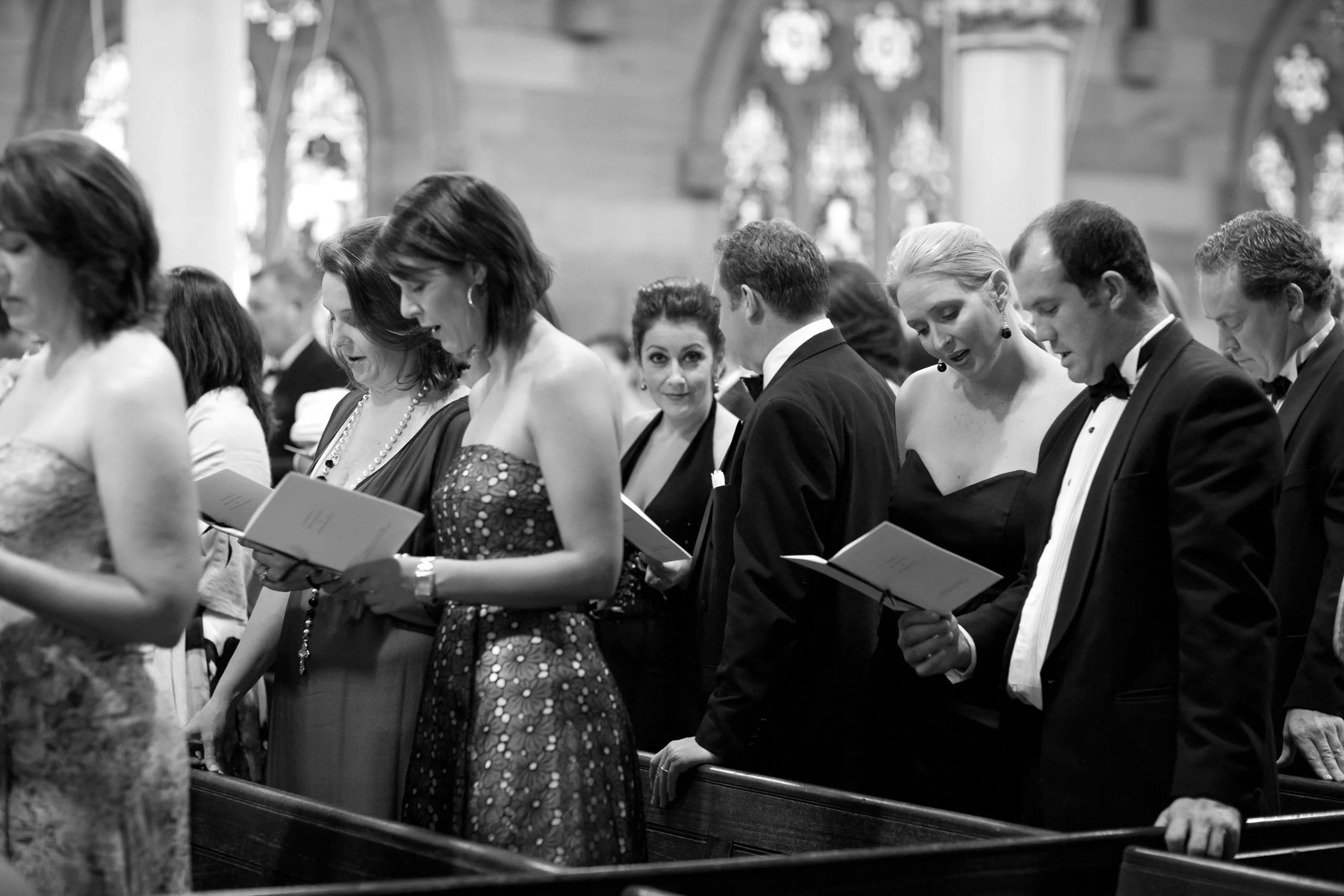 Bridal guests singing with stained glass windows behind them, All Saints Anglican Church Woollahra