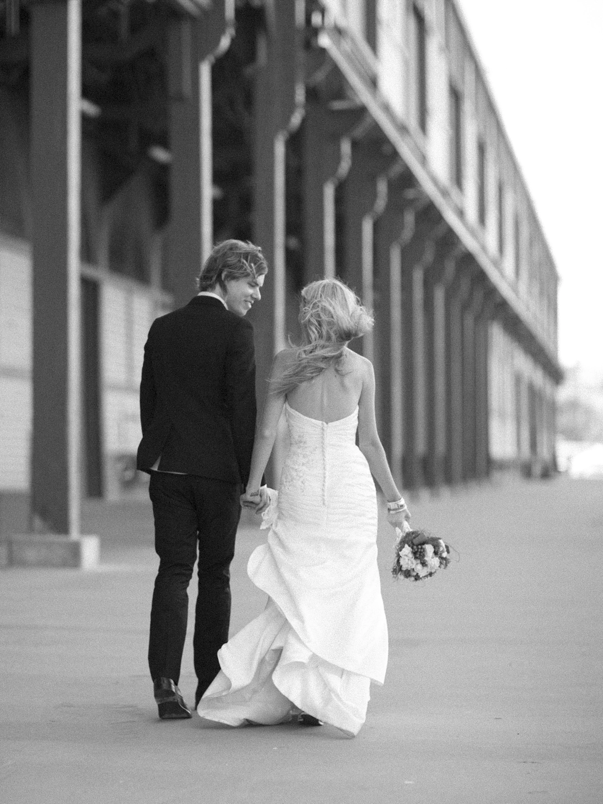 Bride and groom hand in hand walking away on Walsh Bay pier