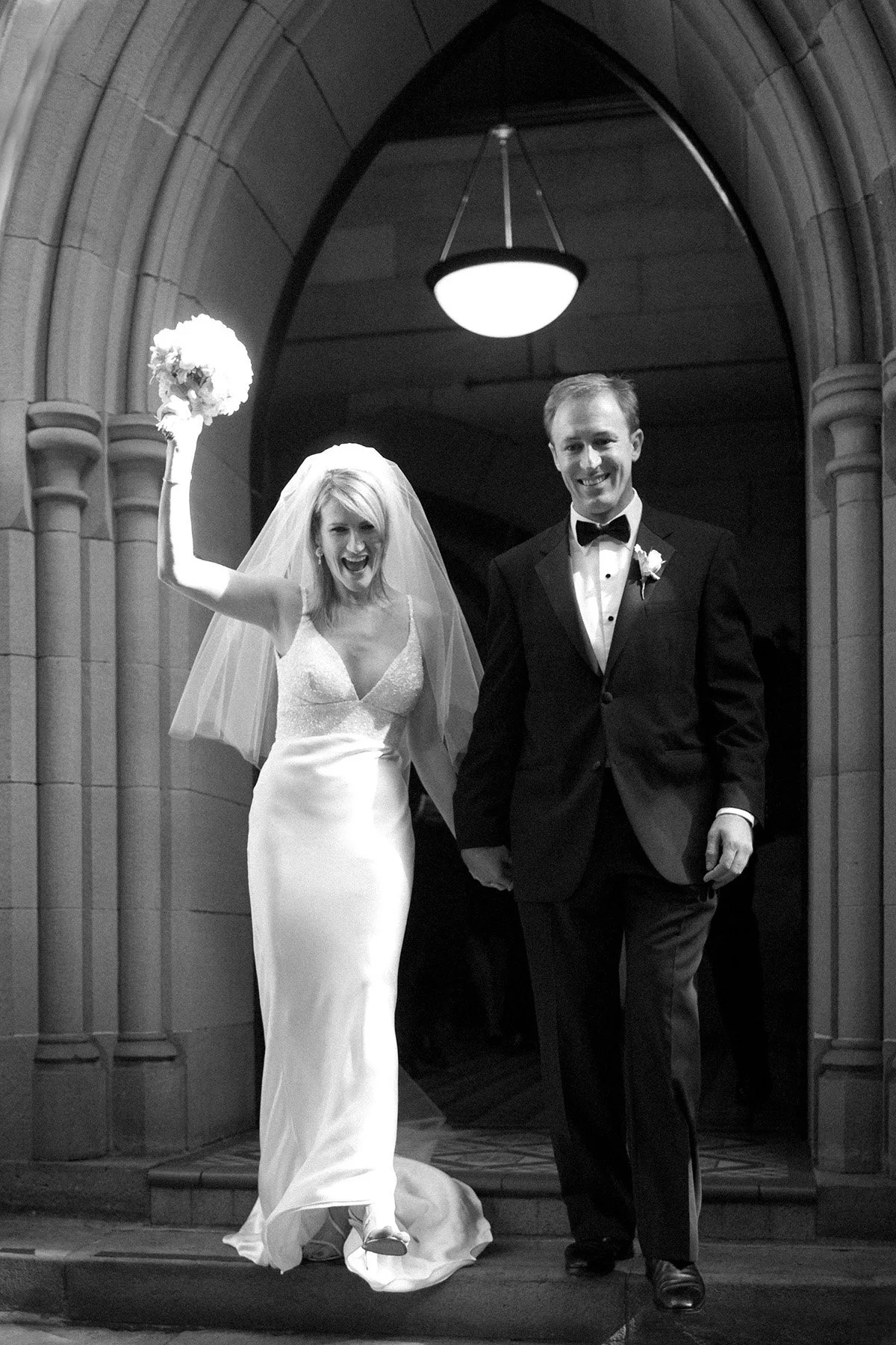 Black and white image of newlyweds walking out through the stone arch of All Saints Anglican Church Woollahra