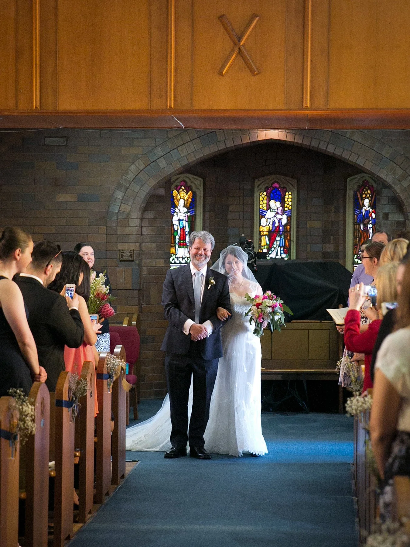 Bride walking down the aisle with stained glass windows behind, St Andrews Anglican Church Roseville