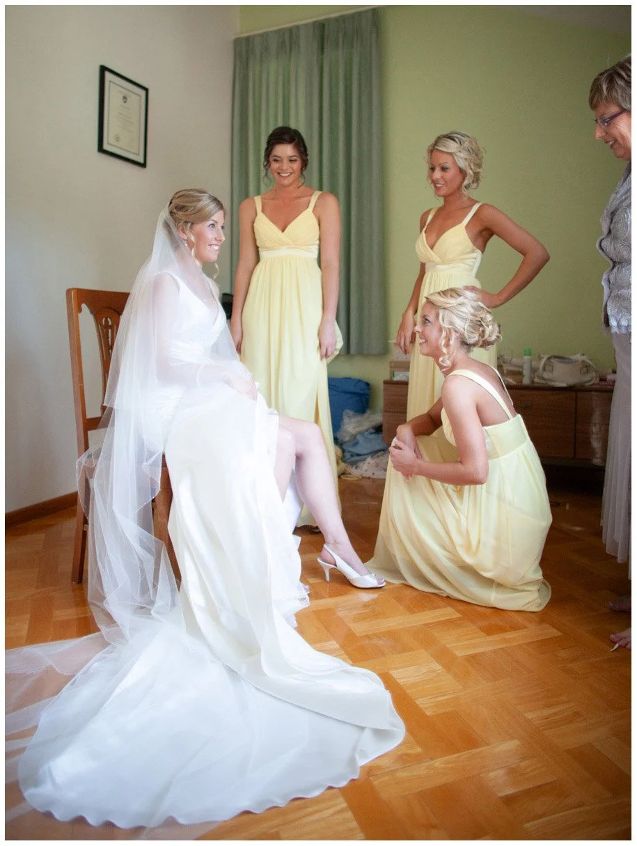 Mother and sisters helping bride with shoe during final wedding preparation