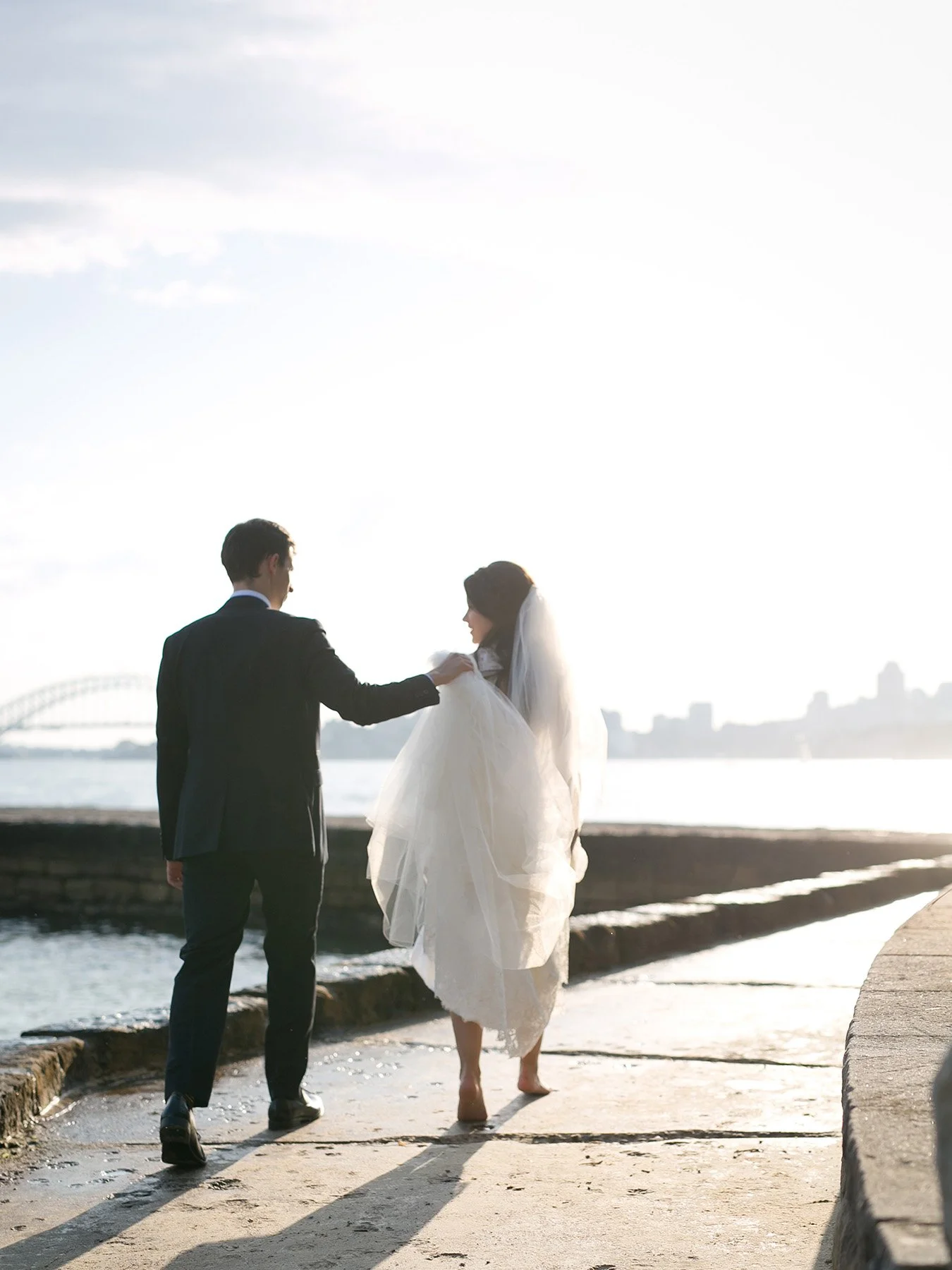Bride and groom walking barefoot on the pavement together at Bradleys Head Mosman