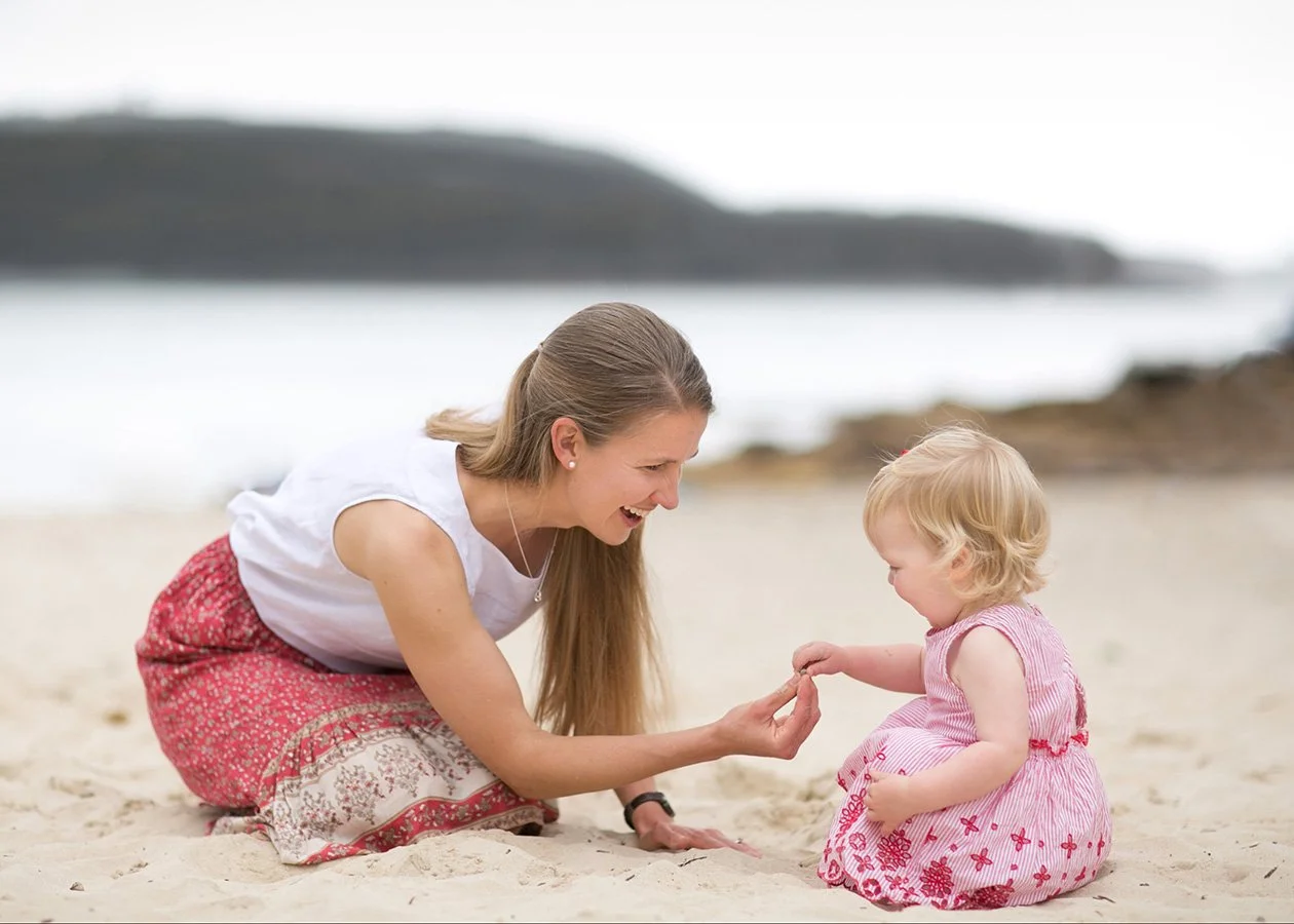 Mother playing in sand with toddler daughter at beach