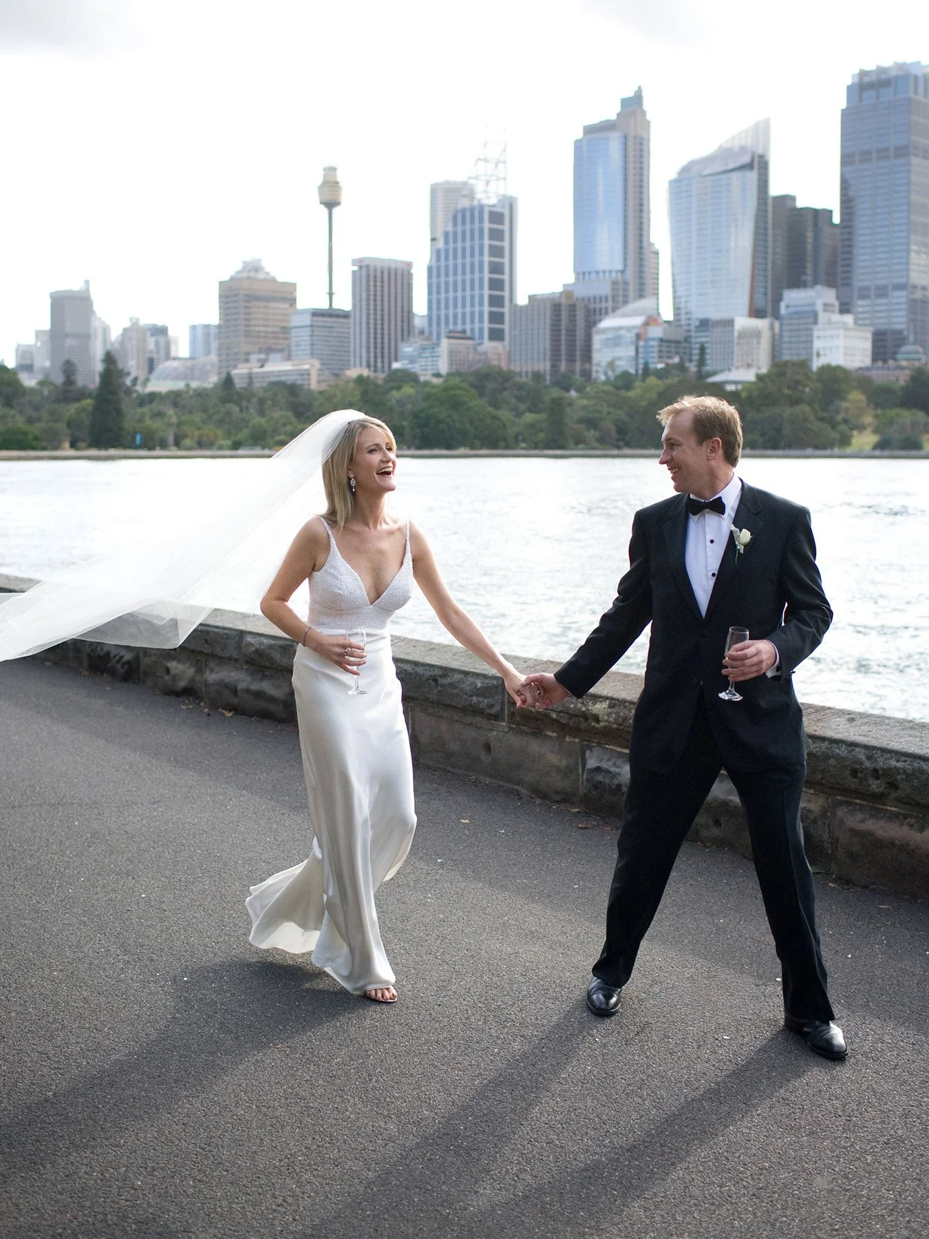 Bride with veil flying and groom laughing with the Sydney CBD skyline behind them, Royal Botanic Gardens