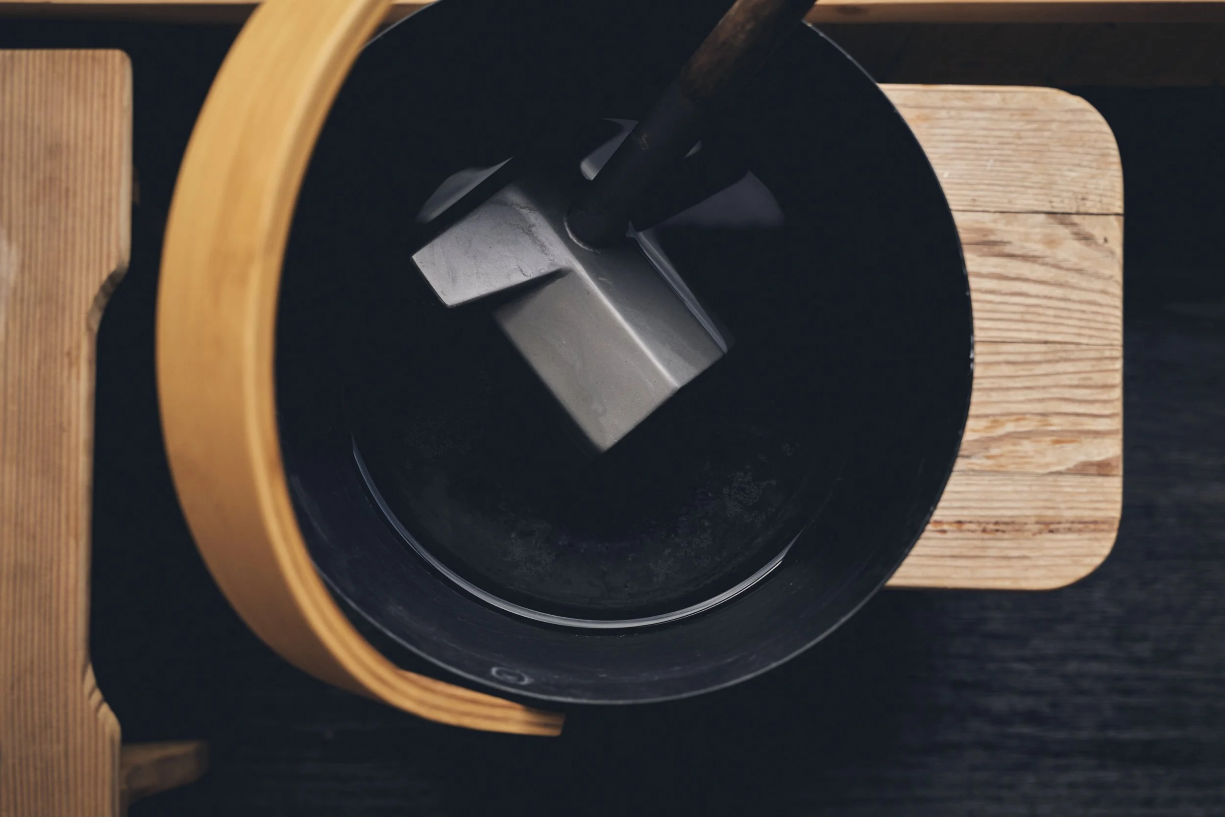 Overhead view of a black mortar and pestle on a wooden cutting board with a dark surface background.
