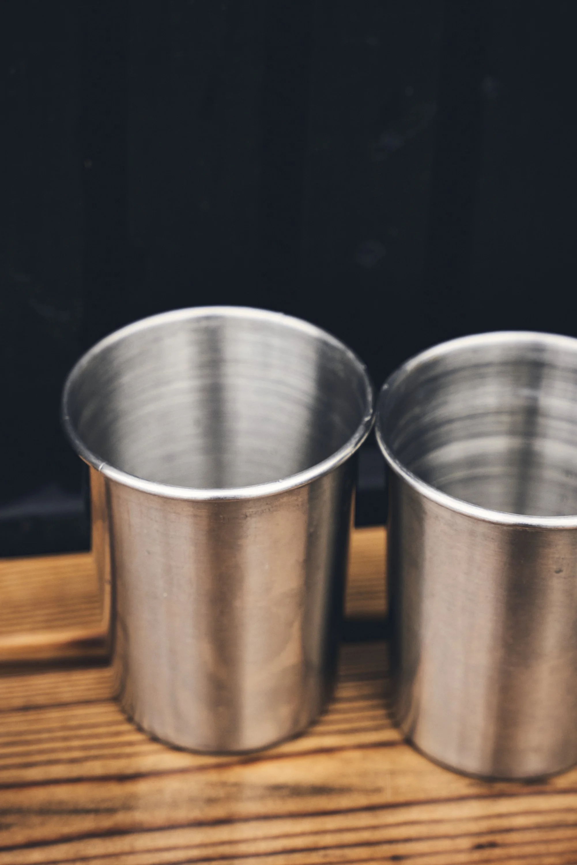Two empty stainless steel cups on a wooden surface with a dark background.