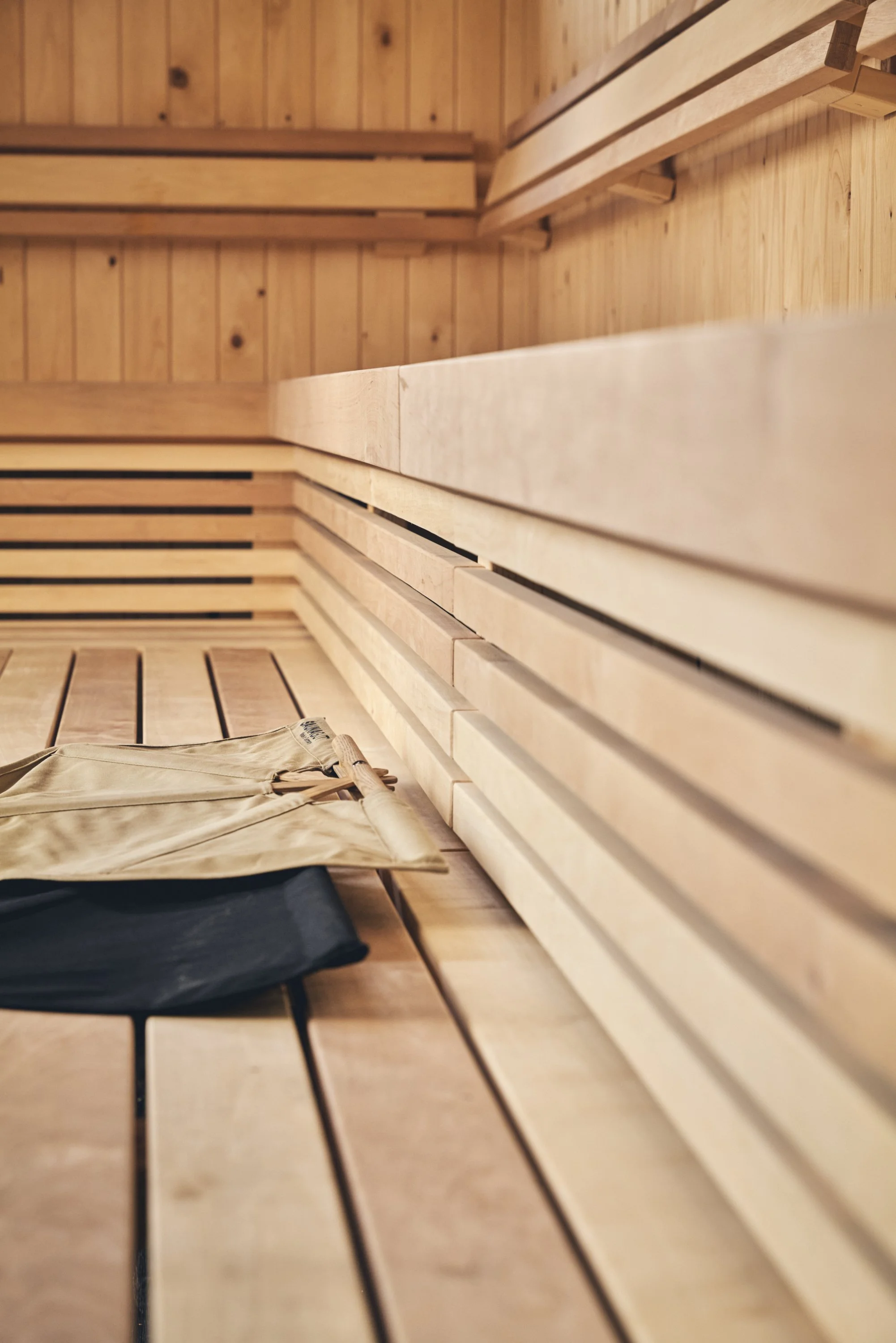 Inside a wooden sauna with benches and a khaki-colored towel and black object on the bench