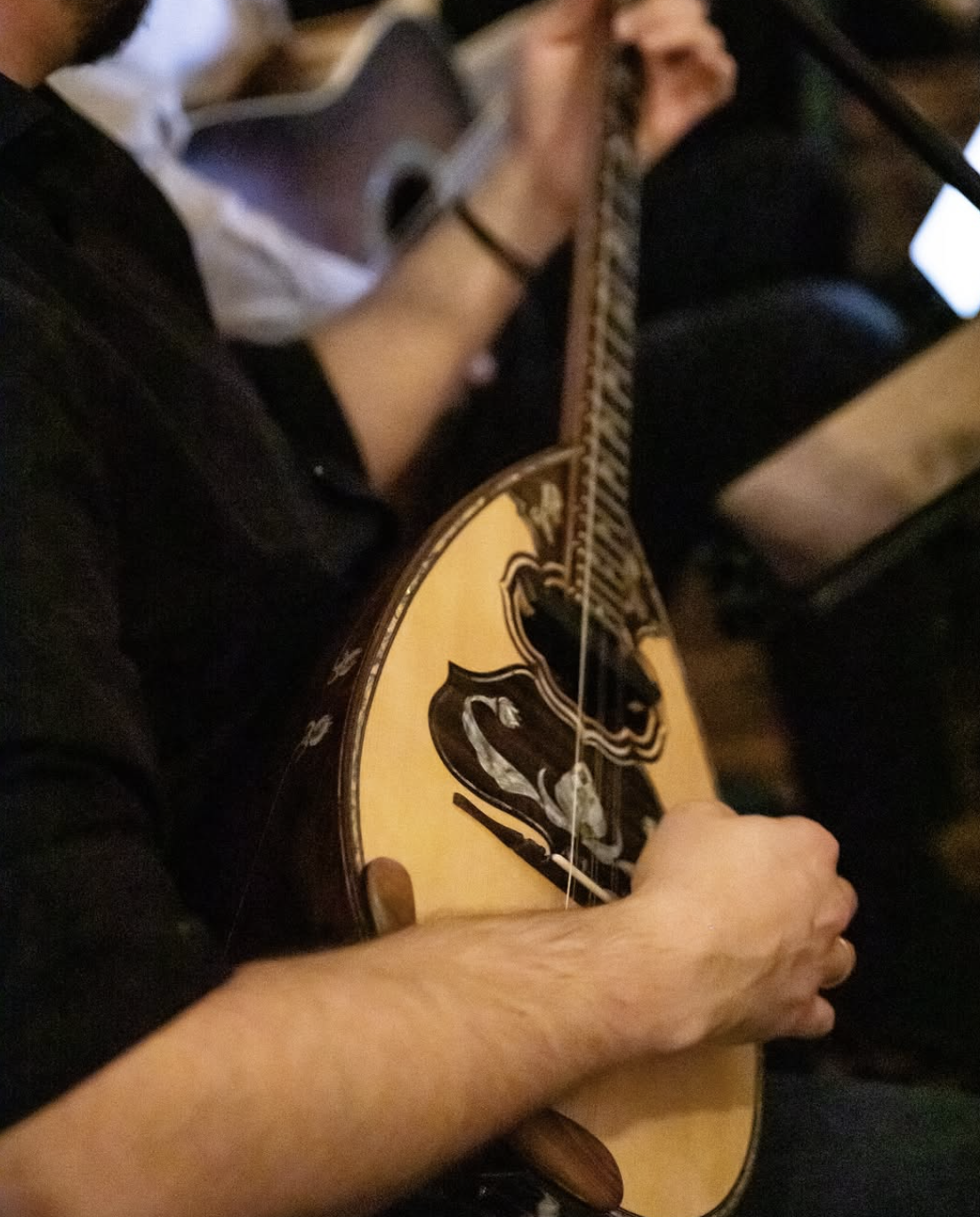 Person playing acoustic guitar with a black and beige design, sitting down, with a lap steel guitar and a smartphone nearby.