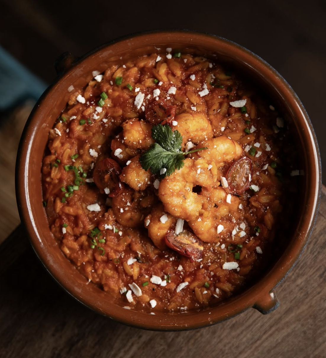 A bowl of shrimp and rice stew garnished with cilantro, chopped onions, and shredded cheese.