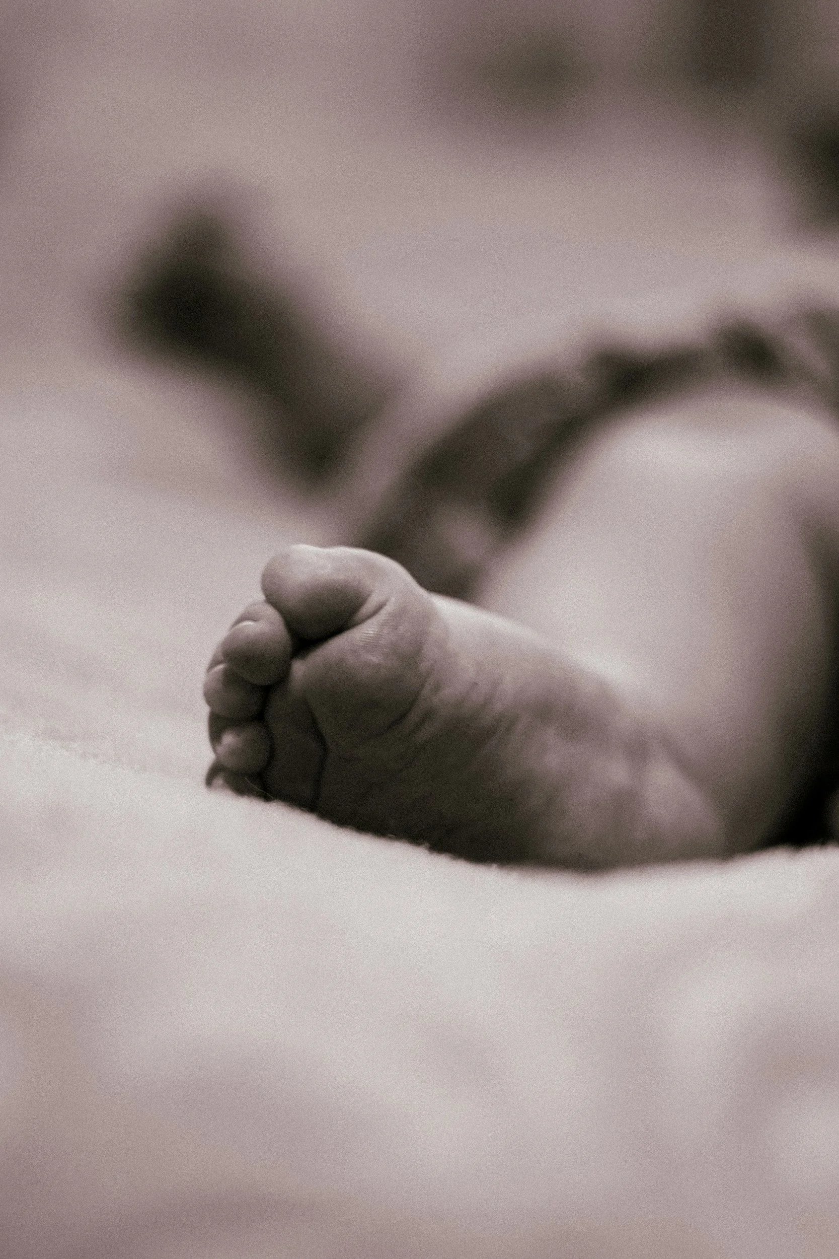 Close-up of a baby's foot on a soft surface, slightly curled toes, with a blurred background.