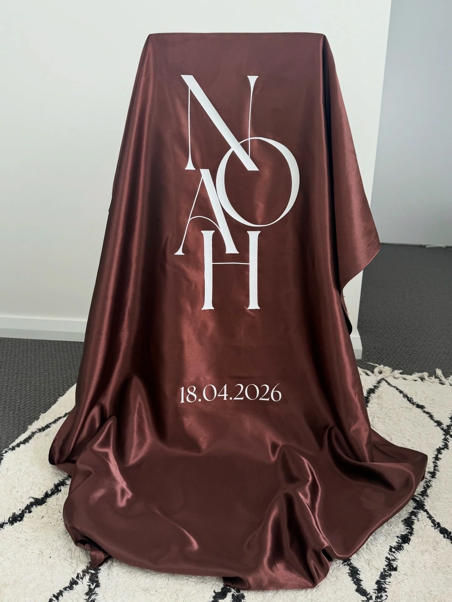 A draped maroon fabric with white overlapping letter design and a date reading 18.04.2026 at the bottom.