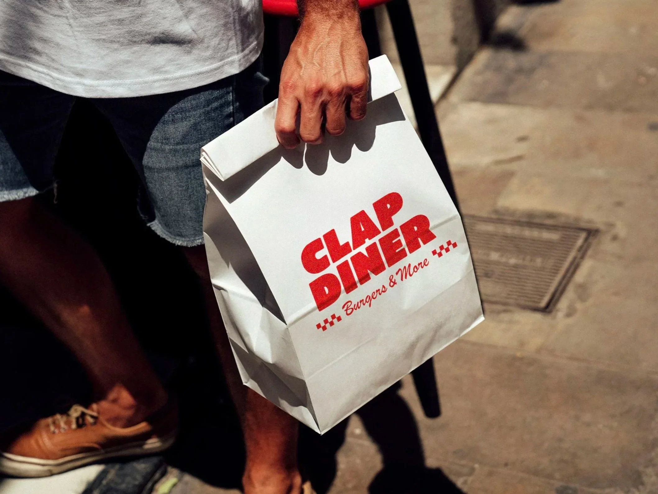 White takeaway paper bag with Clap Diner logo and ‘Burgers & More’ tagline.