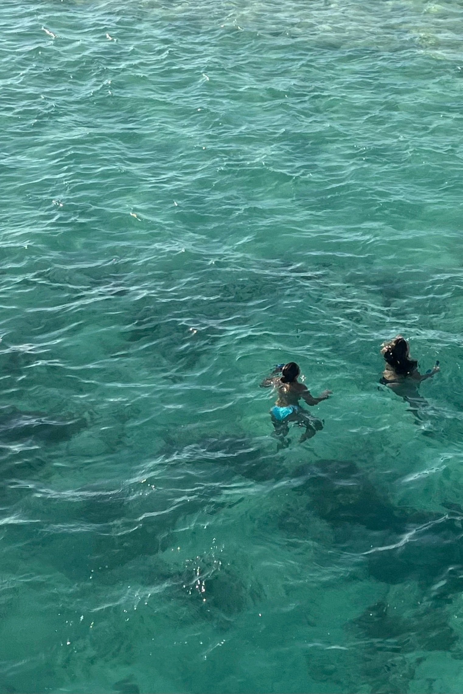 Two children swimming and playing in clear blue water.