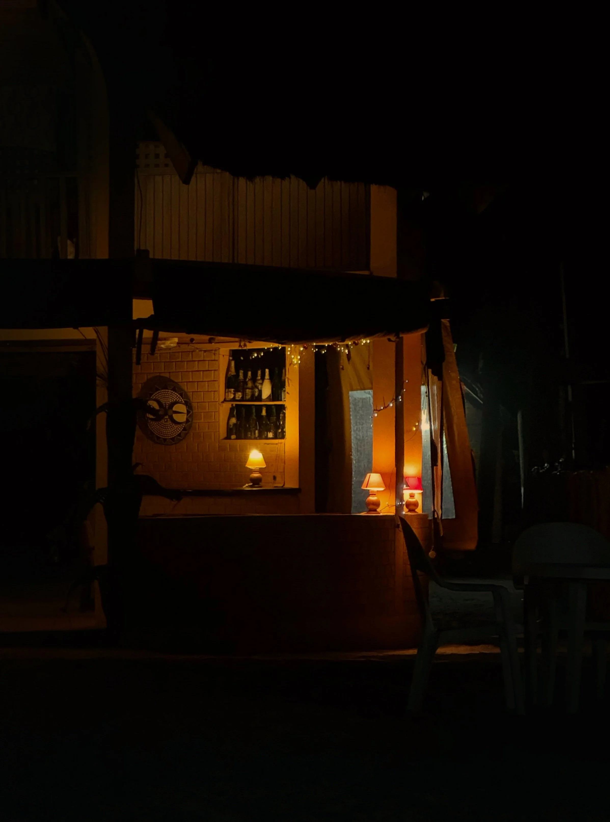 Dimly lit outdoor bar area with small table lamps, chairs, and string lights.