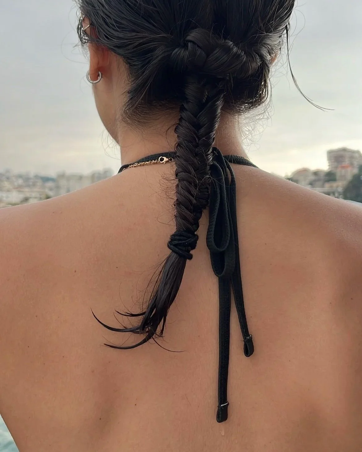 Back view of a woman with braided hair and earrings, photographed outdoors in an urban setting.