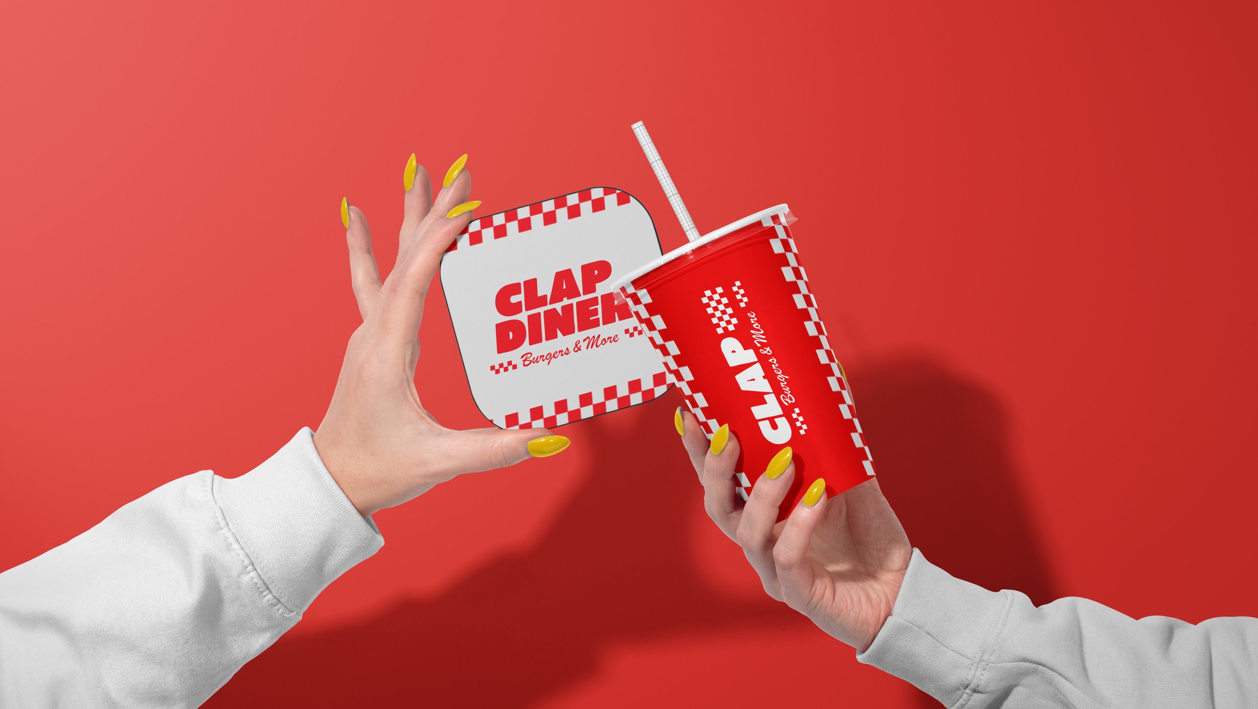 Two hands with yellow nails hold a red and white Clapp Diner cup with a straw and a matching square container, against a red background.