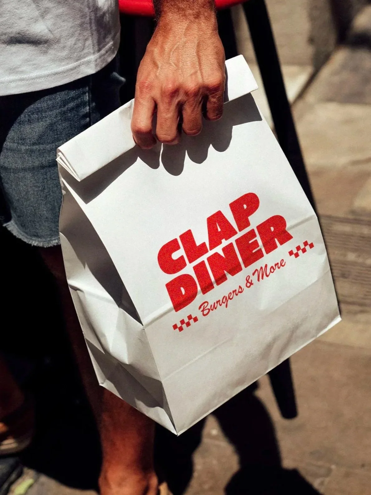 White takeaway paper bag with Clap Diner logo and ‘Burgers & More’ tagline.