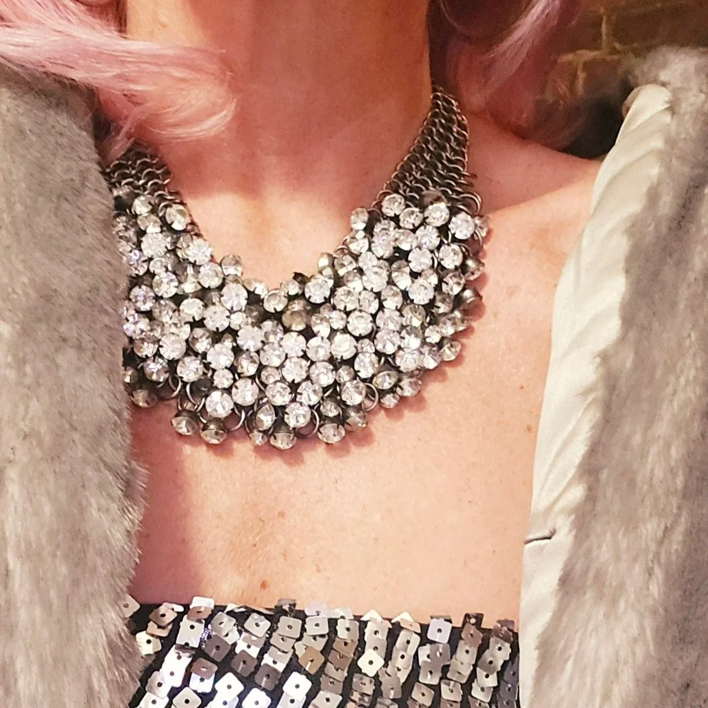 Close-up of a woman's upper torso and neck adorned with a large, statement, rhinestone necklace.