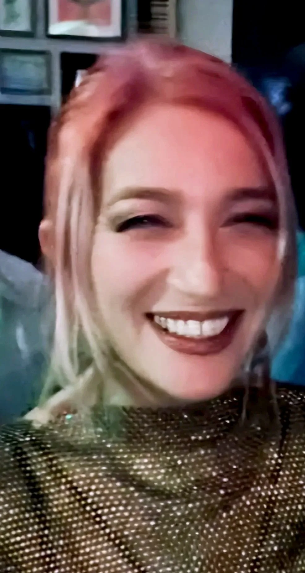 A smiling woman with pink hair wearing a metallic dress