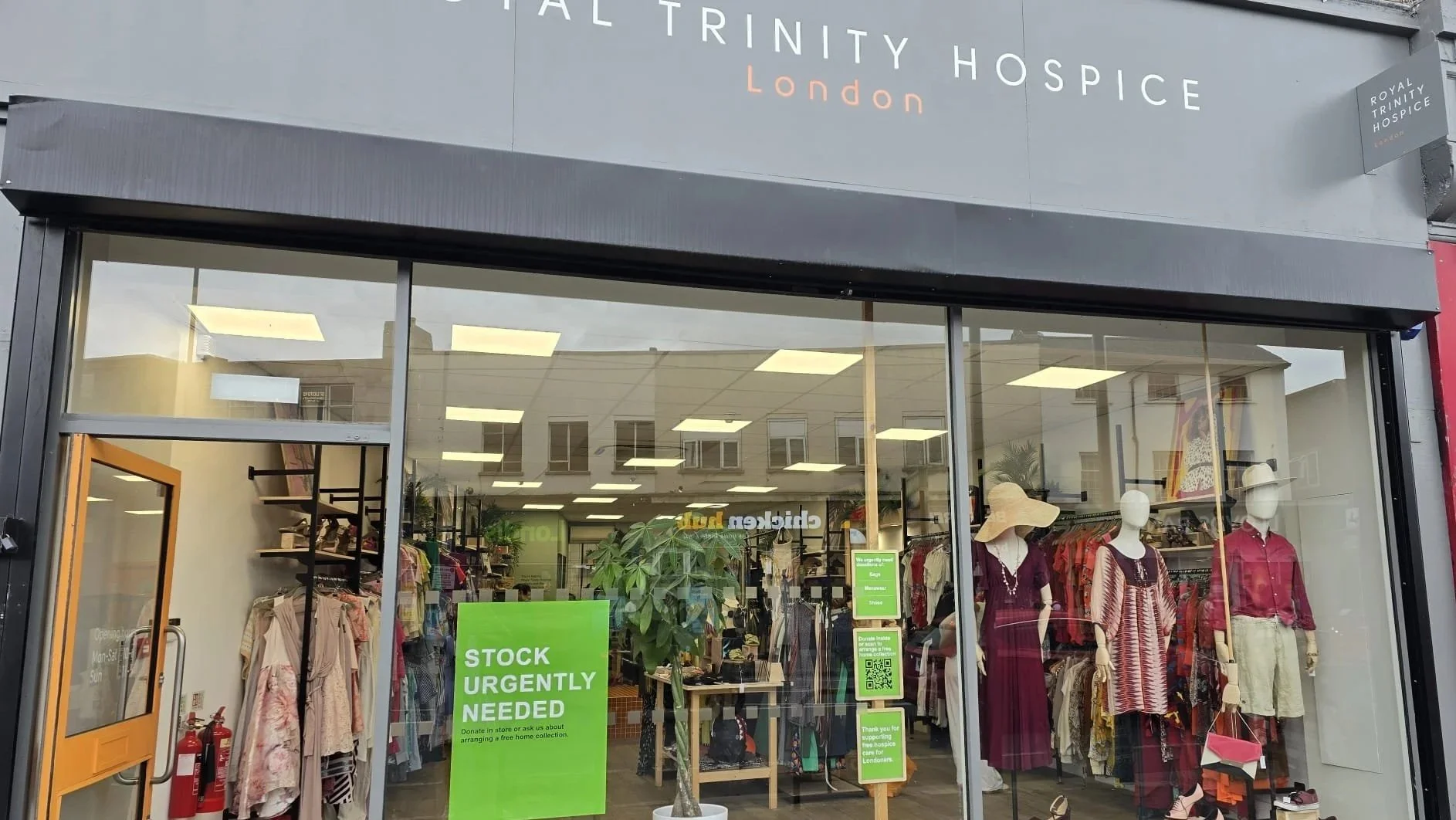 Front view of a Royal Trinity Hospice charity shop with mannequins dressed in hues of red and various second-hand clothes displayed inside.