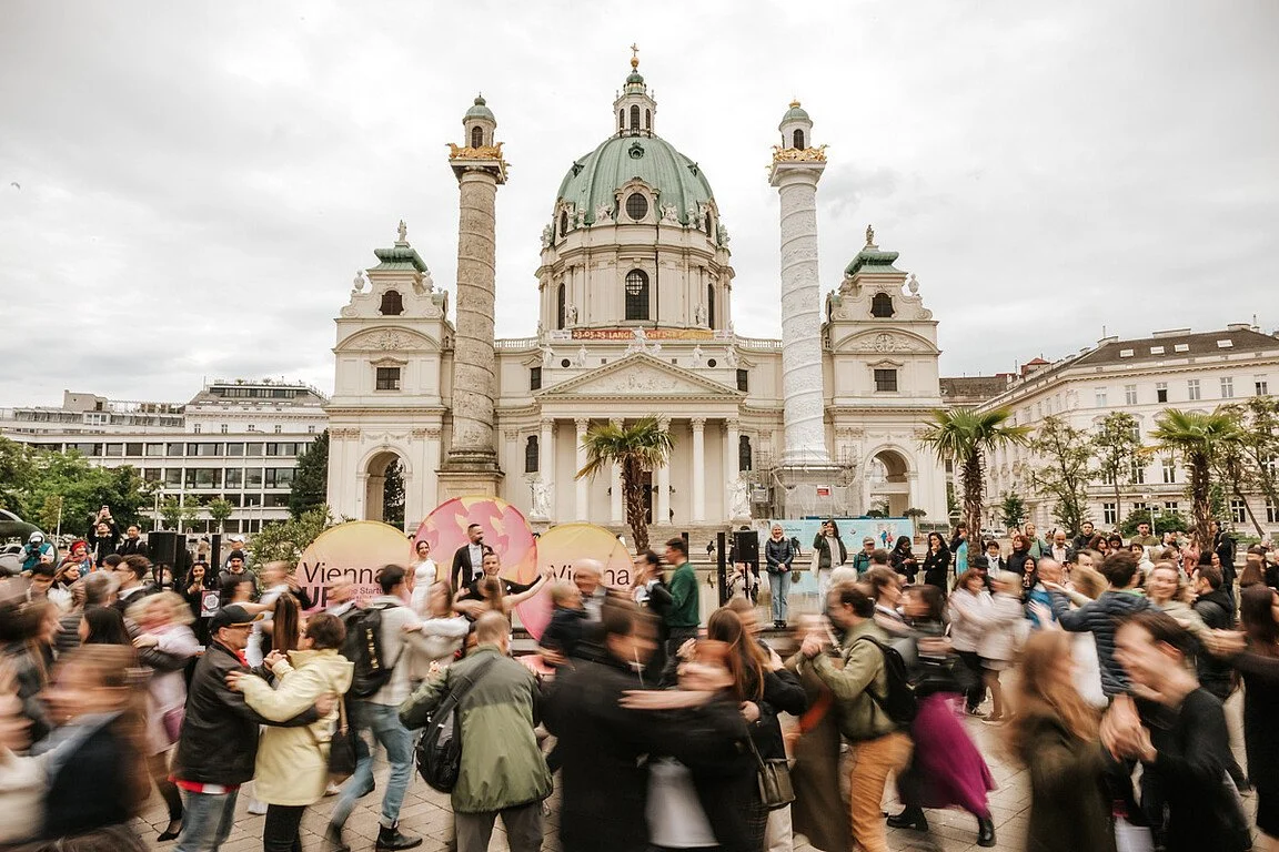 Crowd of people gathered outside the Karlskirche church in Vienna with balloons and event signage