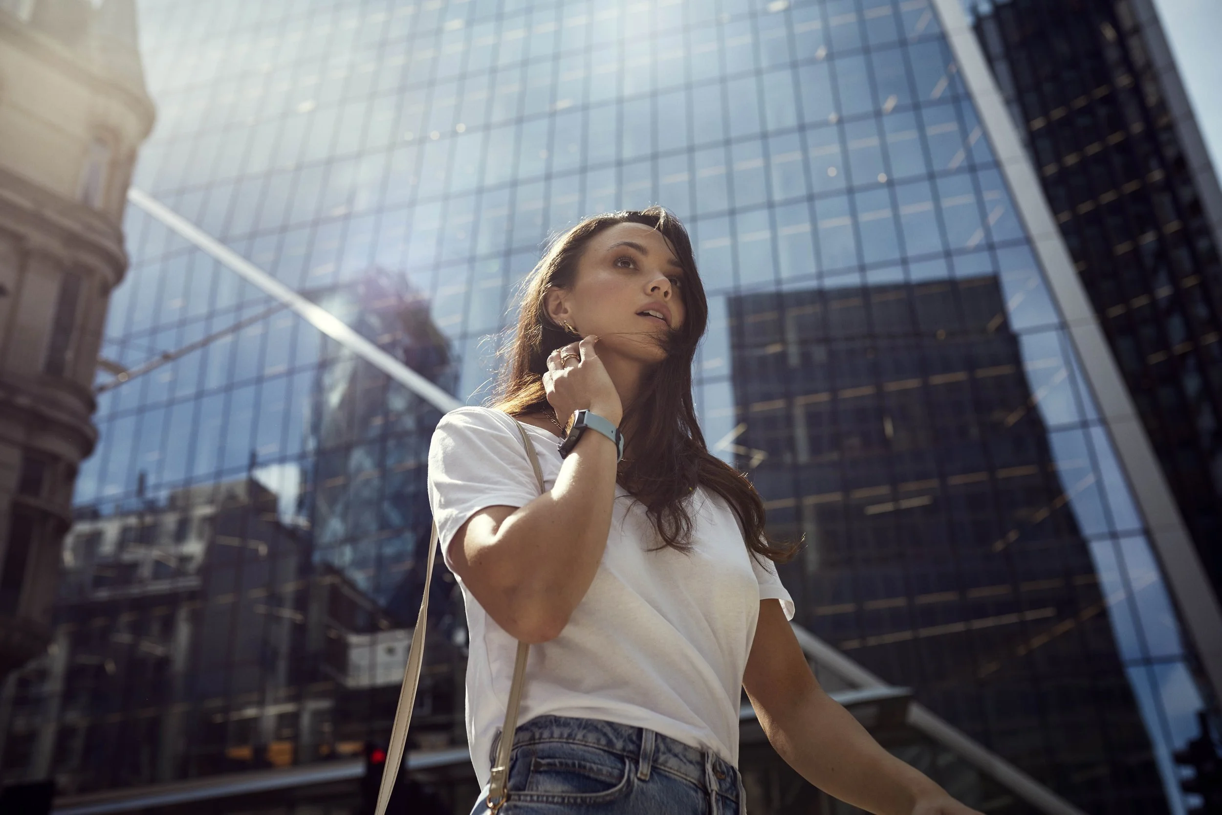 A women wearing a smartwatch walks through the city; past modern glass buildings. Photographer Jon Enoch shot this lifestyle image for tech firm Mobvoi.