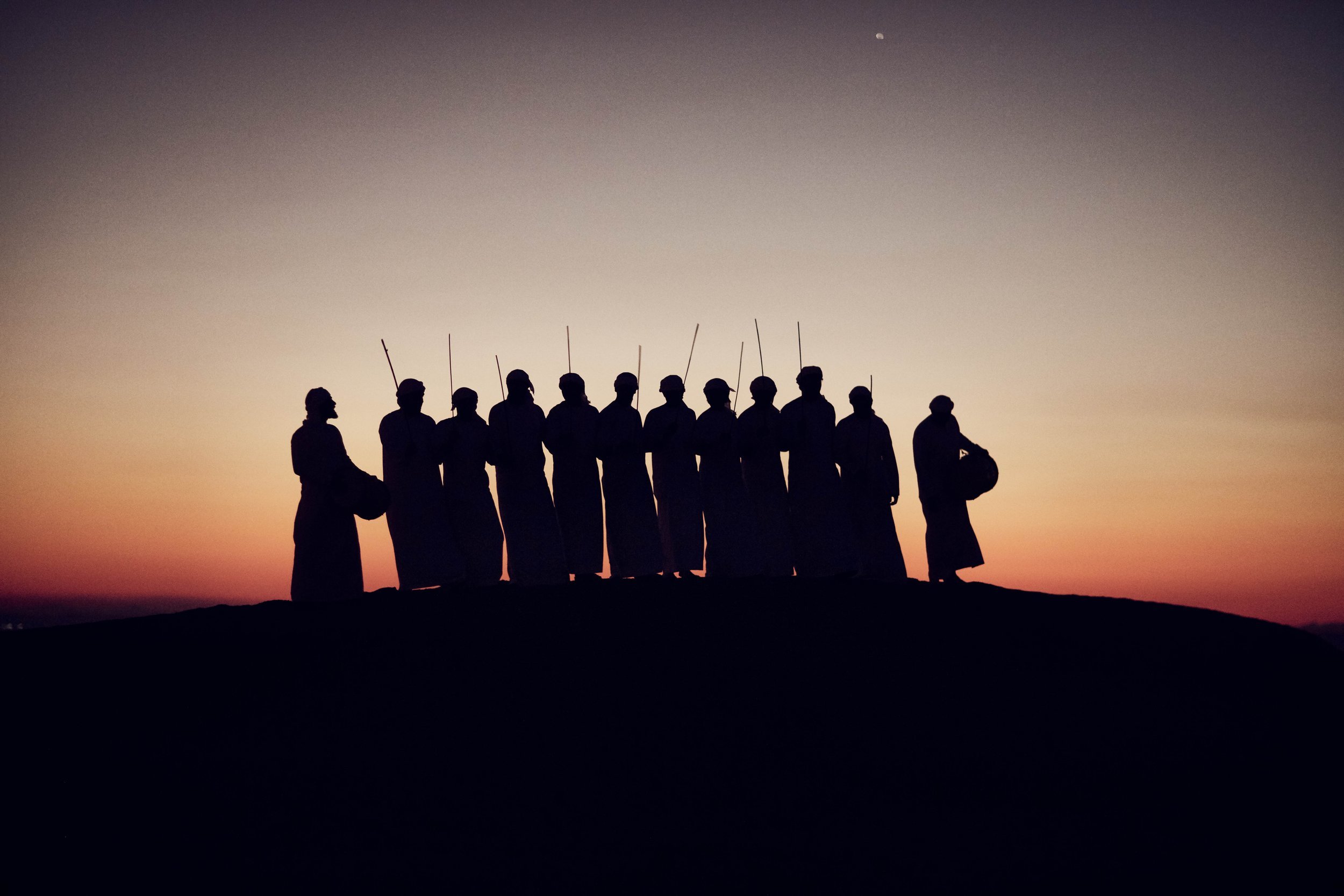 A group of men - silhouetted against the sun in the Dubai desert in this advertising lifestyle image by photographer Jon Enoch