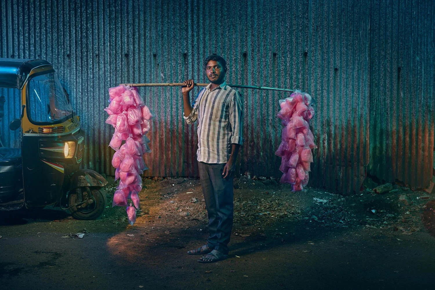 A man stands next to a rickshaw holding a display of cotton candy in Mumbai, India in this photography taken by advertising photographer Jon Enoch.