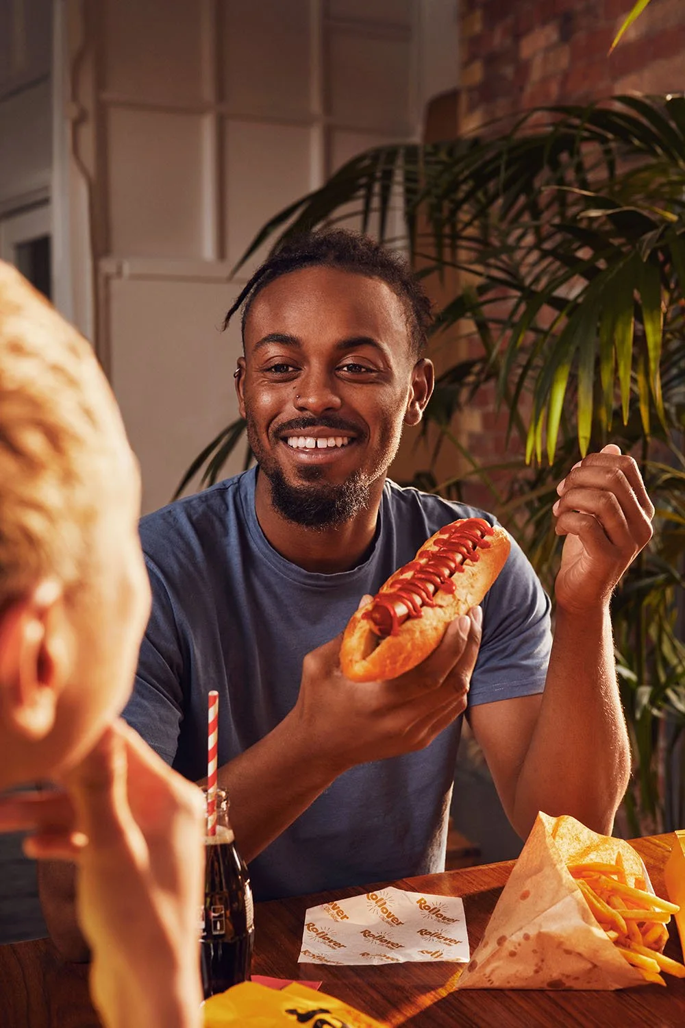 A man chats to his friends whilst eating a hotdog in this lifestyle image taken by London based Jon Enoch